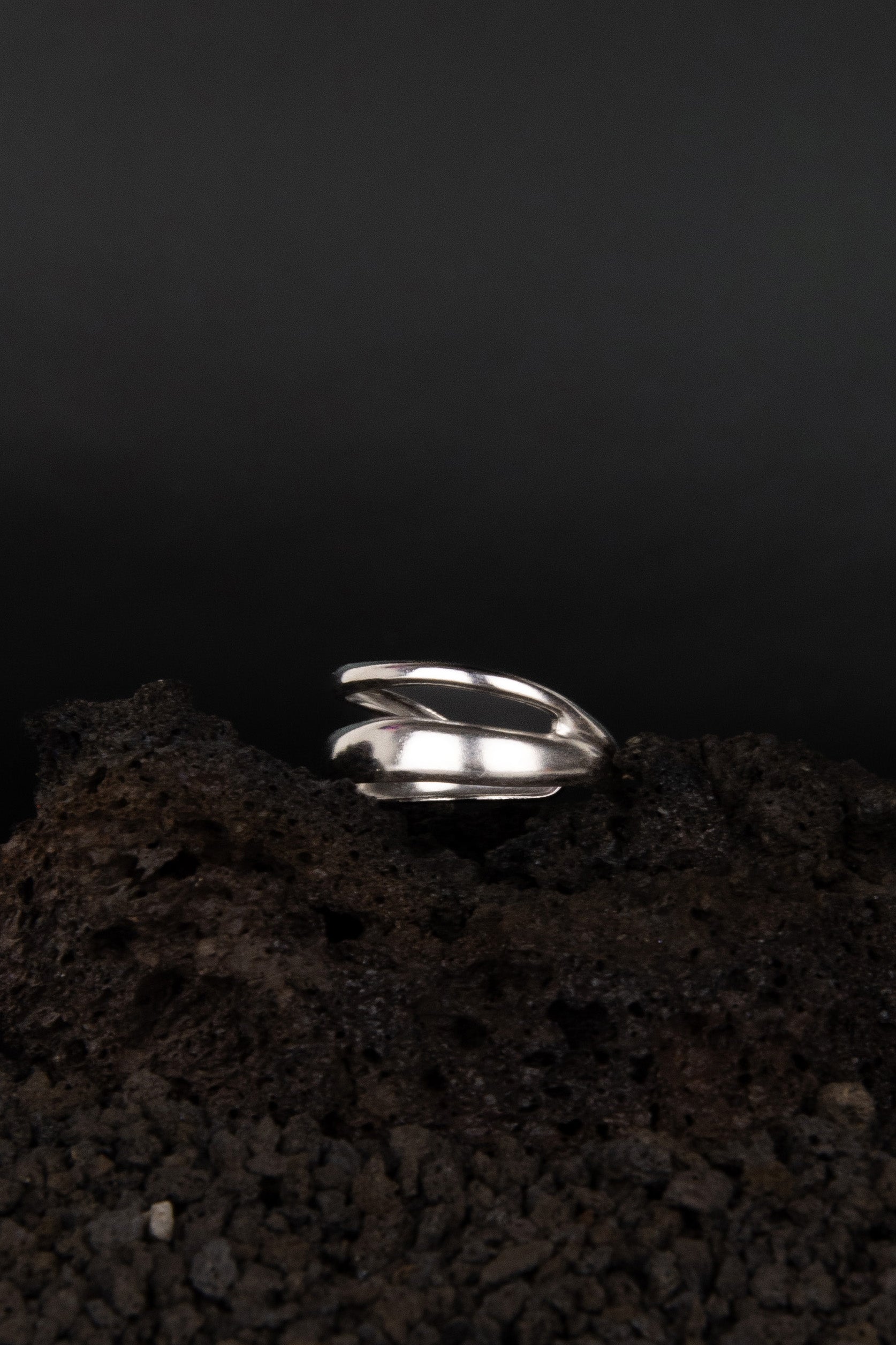Bague ouverte en acier inoxydable  de mise en scène sur une roche volcanique noir et posé de trois quarts.