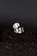Bague en acier inoxydable avec une texture similaire au bois coupé posée sur de la roche volcanique noir.