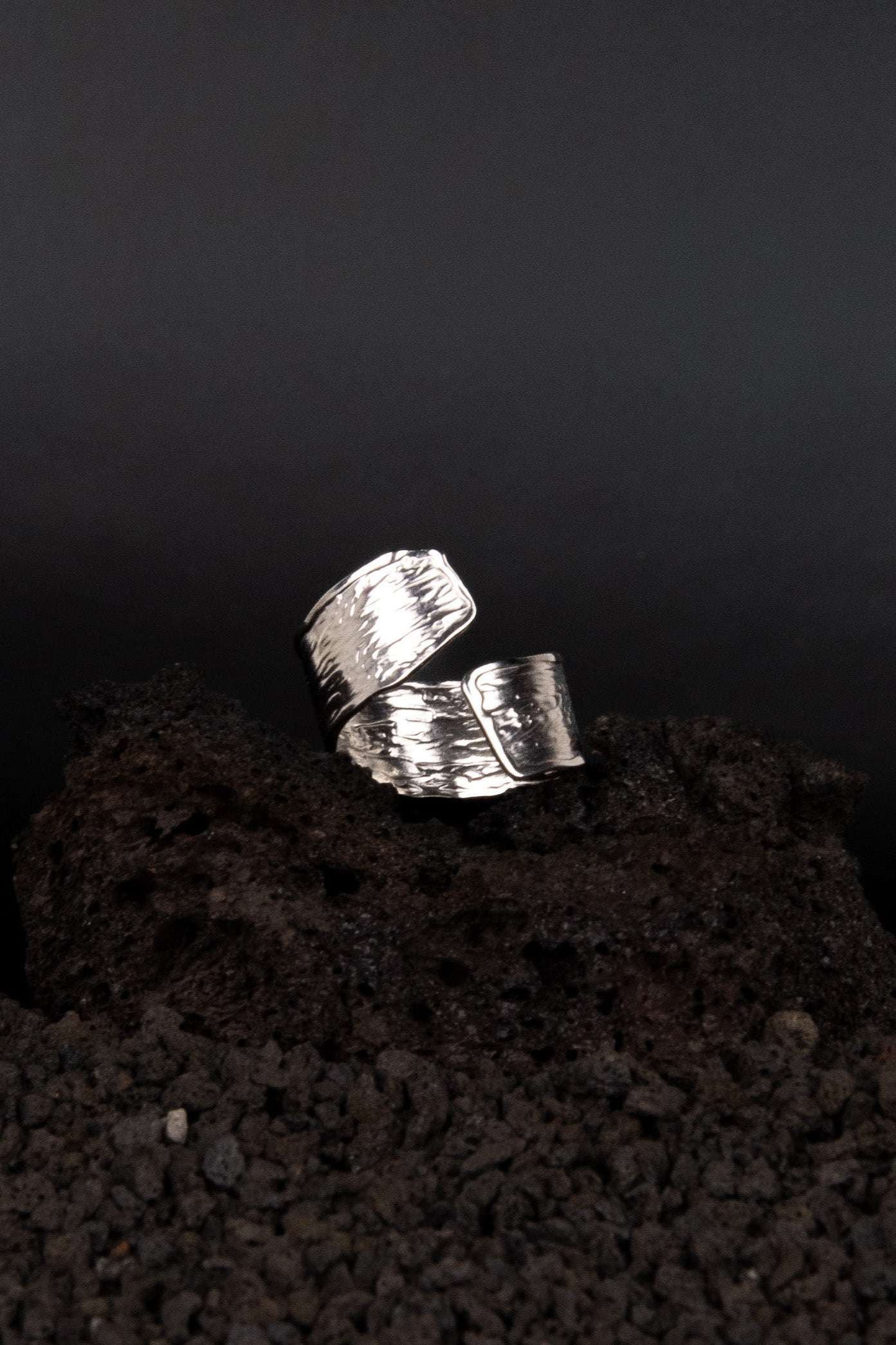 Bague en acier inoxydable avec une texture similaire au bois coupé posée sur de la roche volcanique noir.