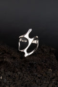 Bague en acier inoxydable en forme de vague métalique posée sur une roche volcanique noir.