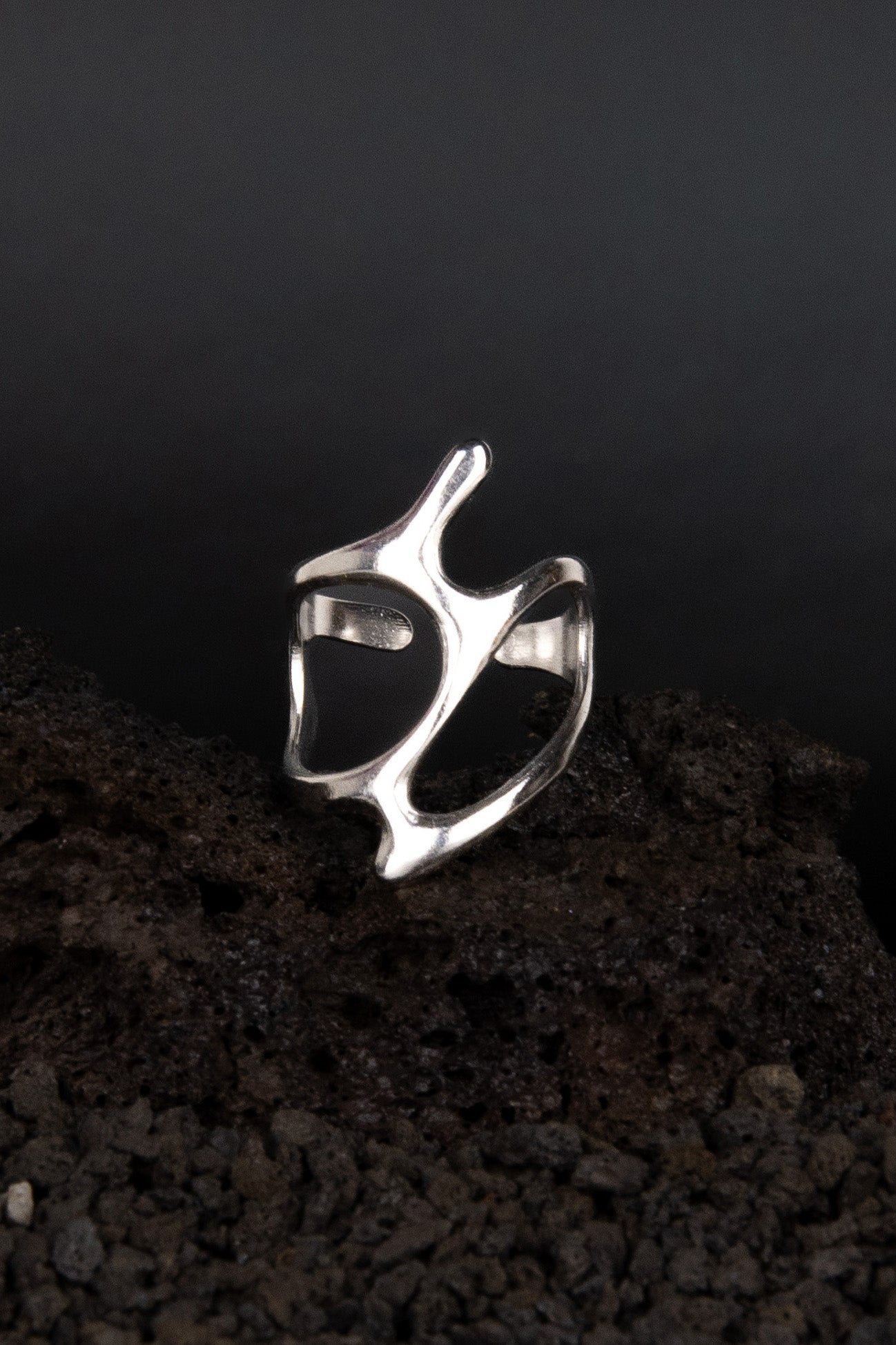 Bague en acier inoxydable en forme de vague métalique posée sur une roche volcanique noir.