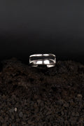 Bague ouverte ajustable en acier inoxydable posée sur de la roche volcanique noir.