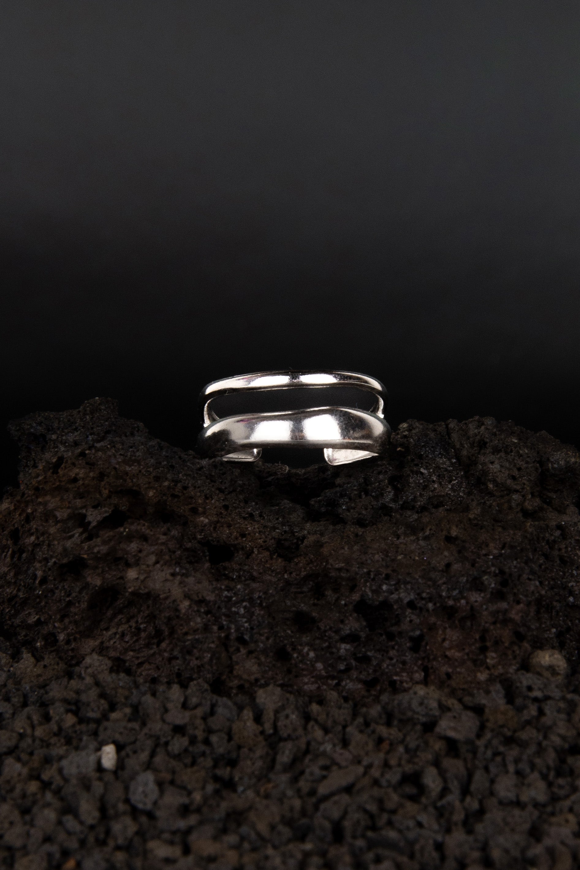 Bague ouverte ajustable en acier inoxydable posée sur de la roche volcanique noir.