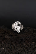bague réglable en acier inoxydable effet métal fondu posé sur de la roche volcanique noir.