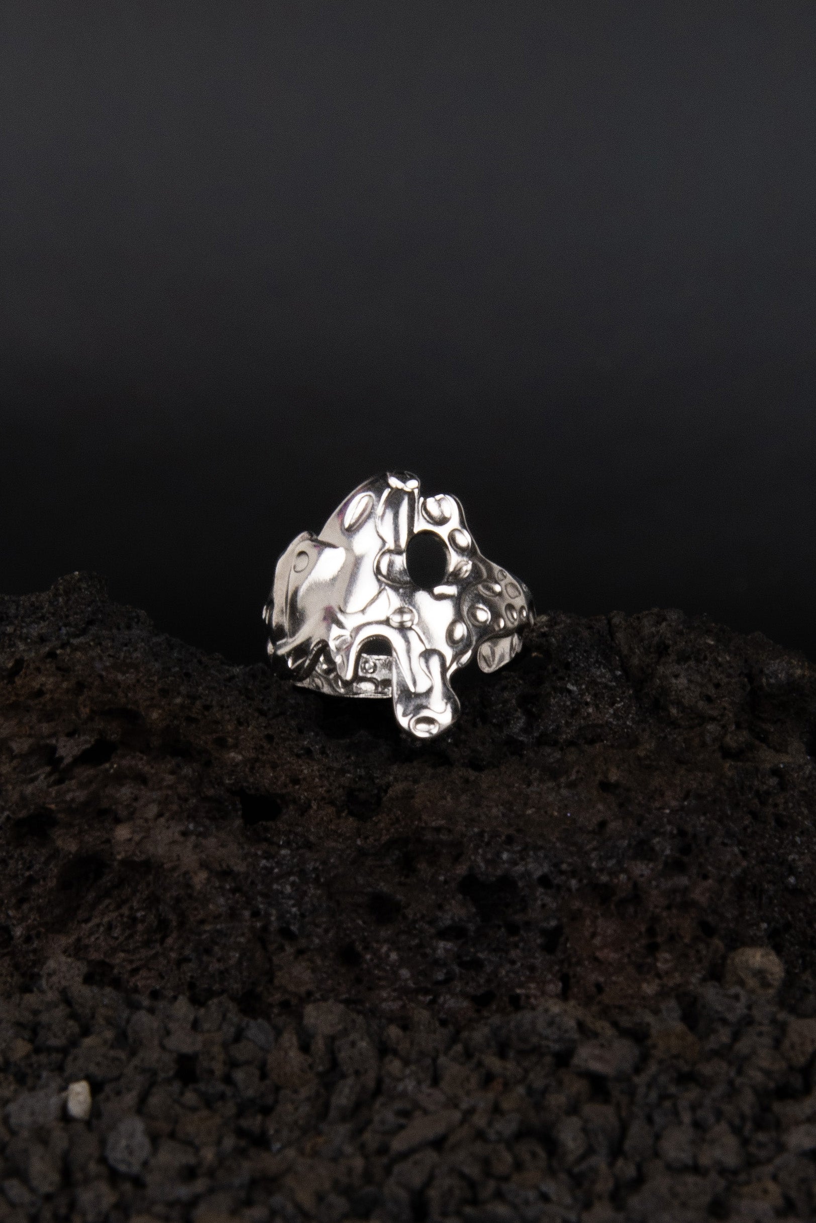 bague réglable en acier inoxydable effet métal fondu posé sur de la roche volcanique noir.
