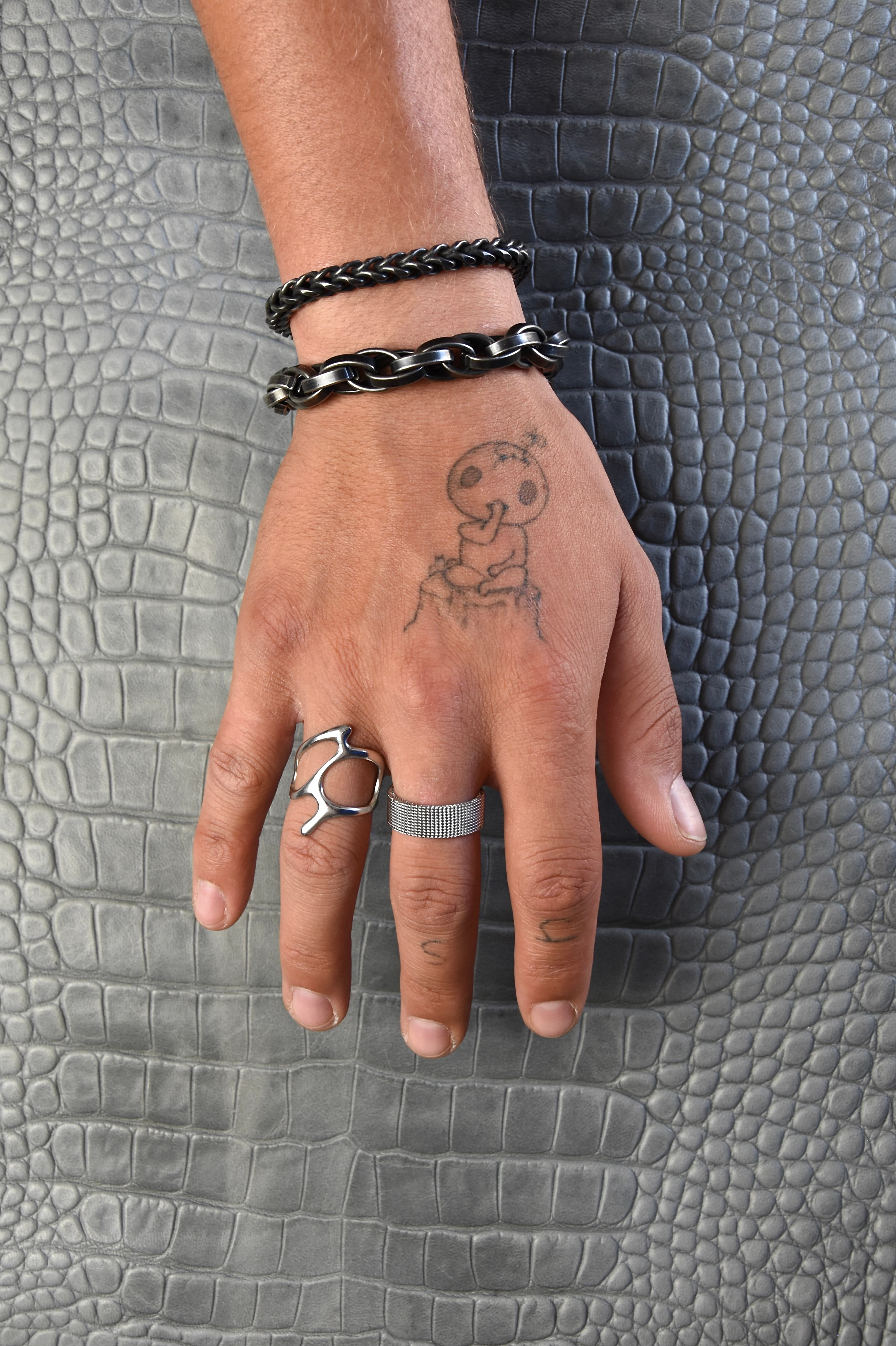 Main portant des bijoux en acier inoxydable par dessus un cuir imitation croco gris.