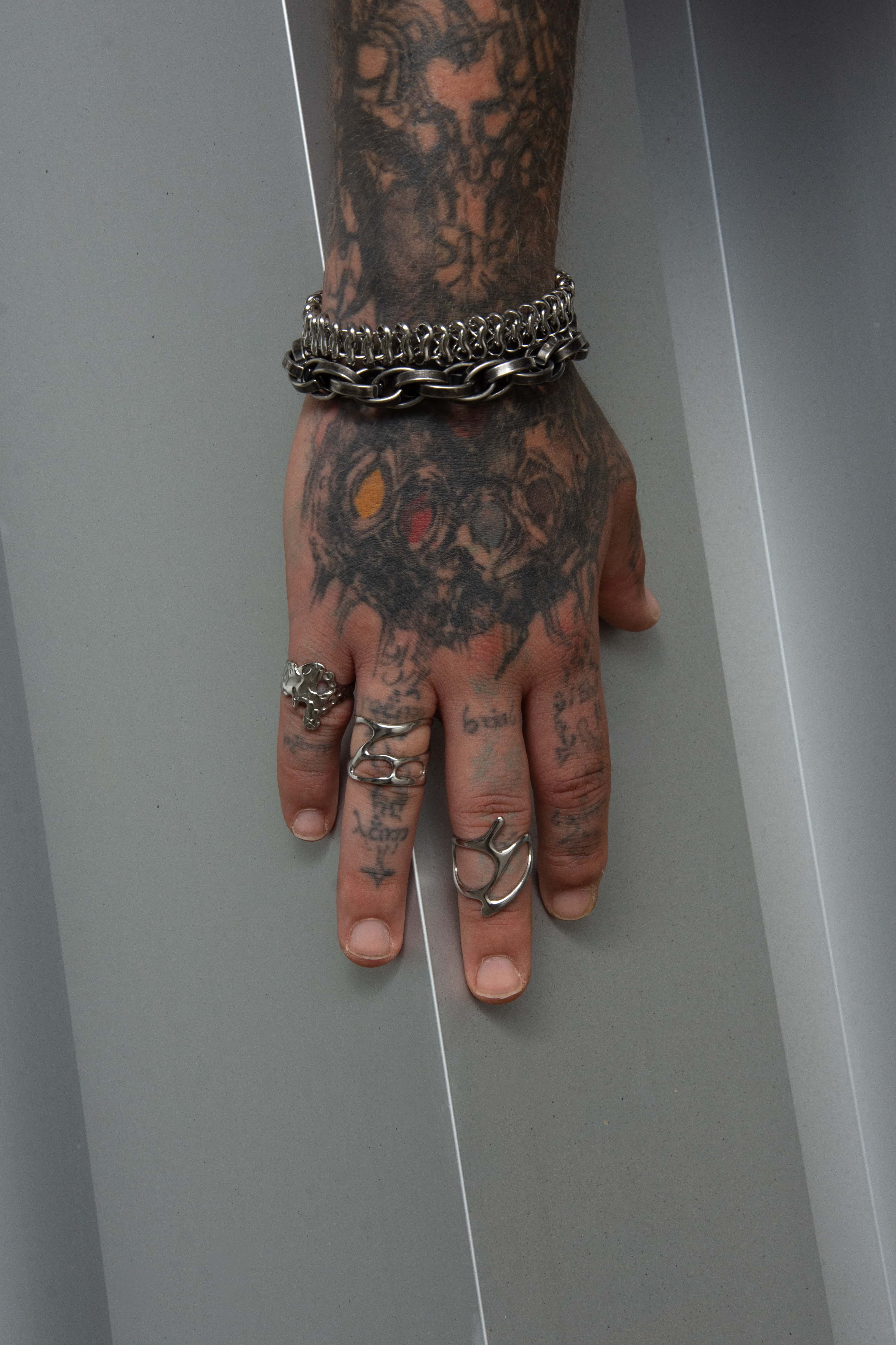 main tatoué portant en ensemble de bijoux au style alternatif en acier inoxydable.