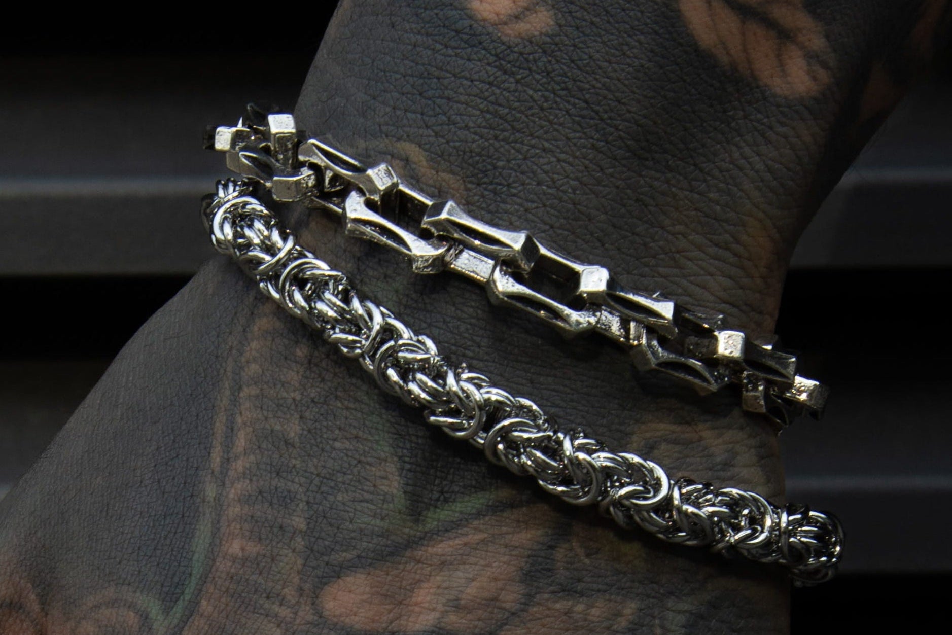 Main tatoué portant bracelet et bagues en acier inoxydable style rock metal alternatif