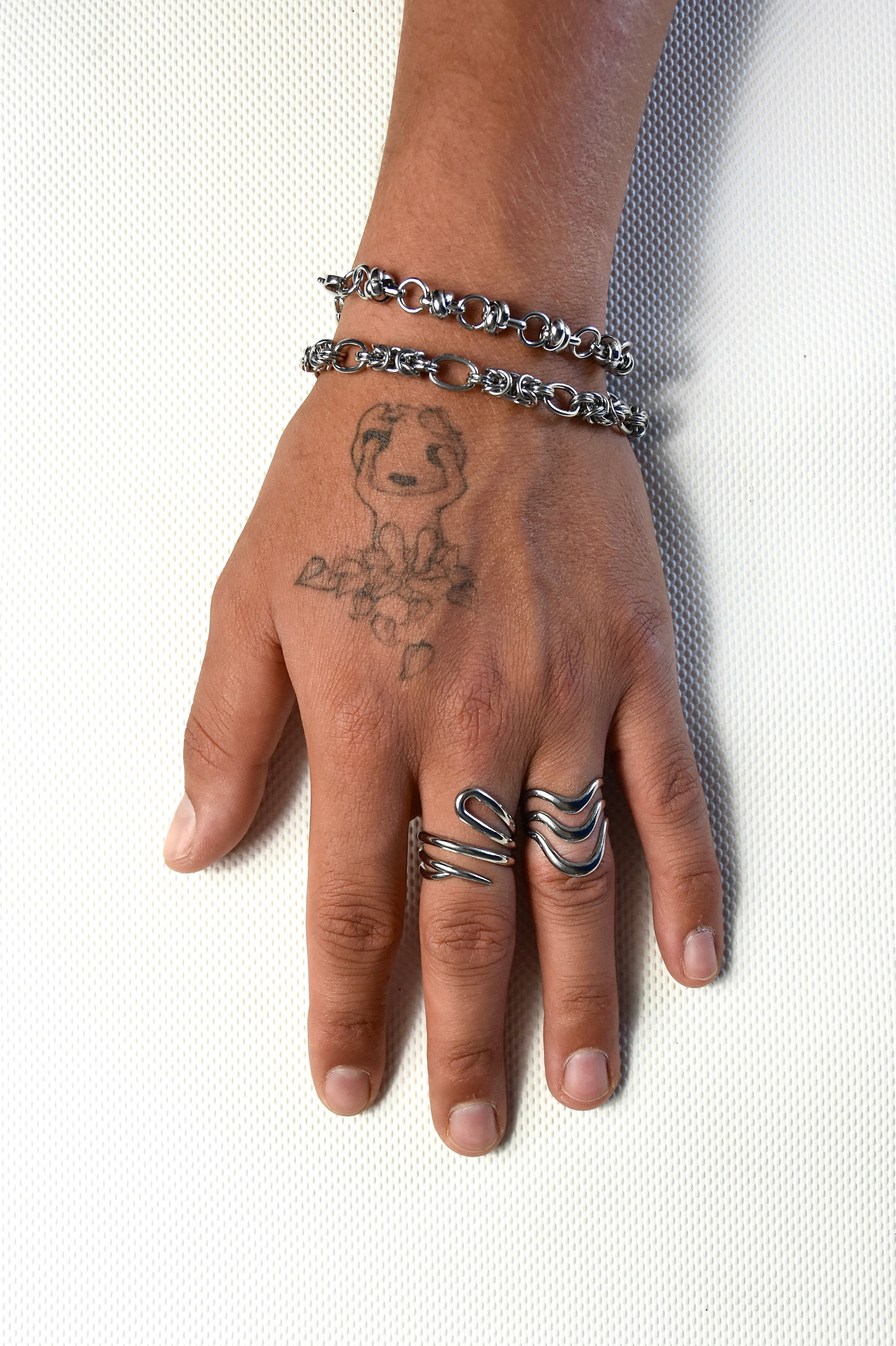 duo de bagues et de bracelet assortie porté par une main tatouée sur fond texturé blanc.