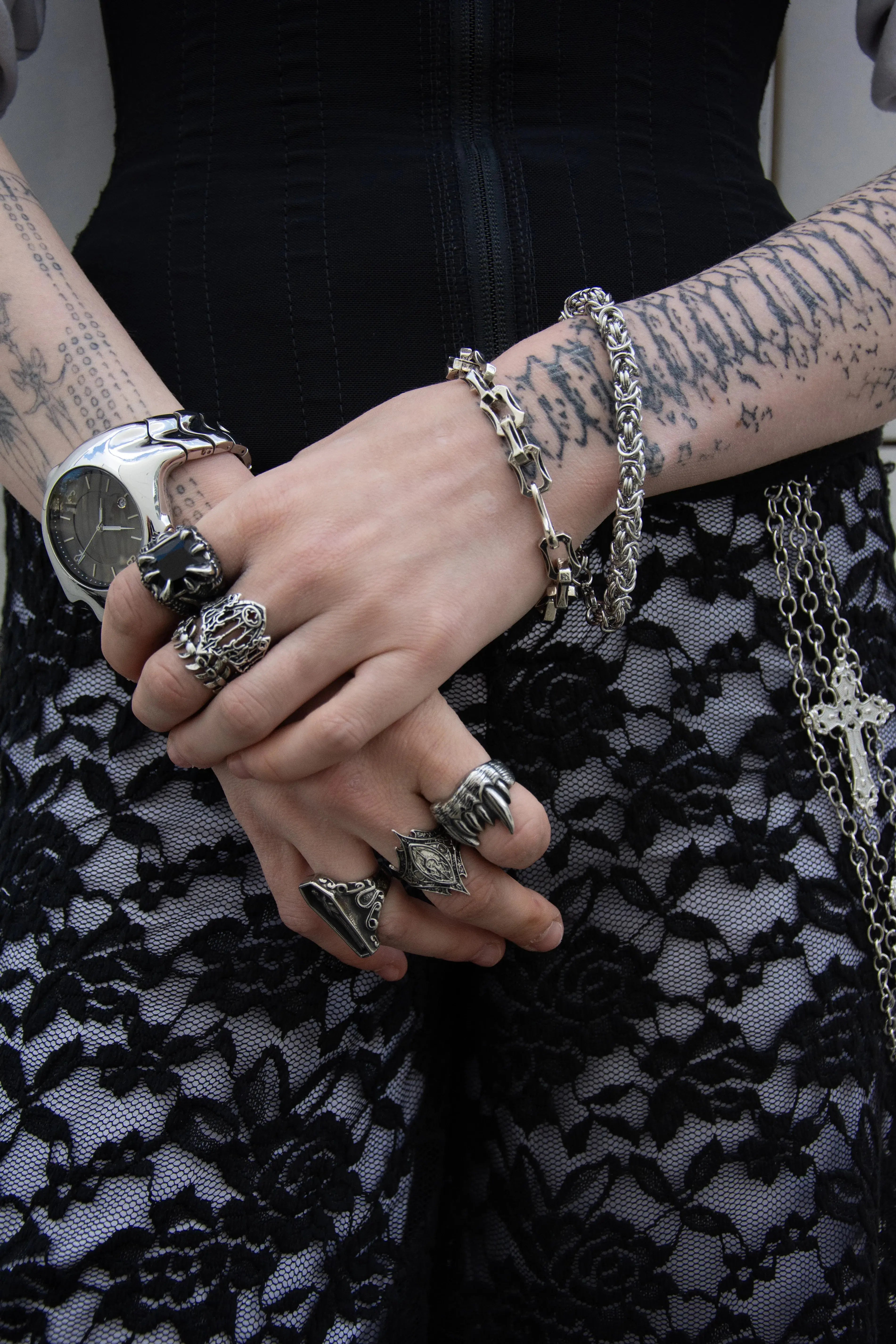 Main de femme portant un bague couronne royal et d'autre bague style alternatif et rock, bague cathédrale, bague squelette, bracelets chaine biker et chaine lacé.