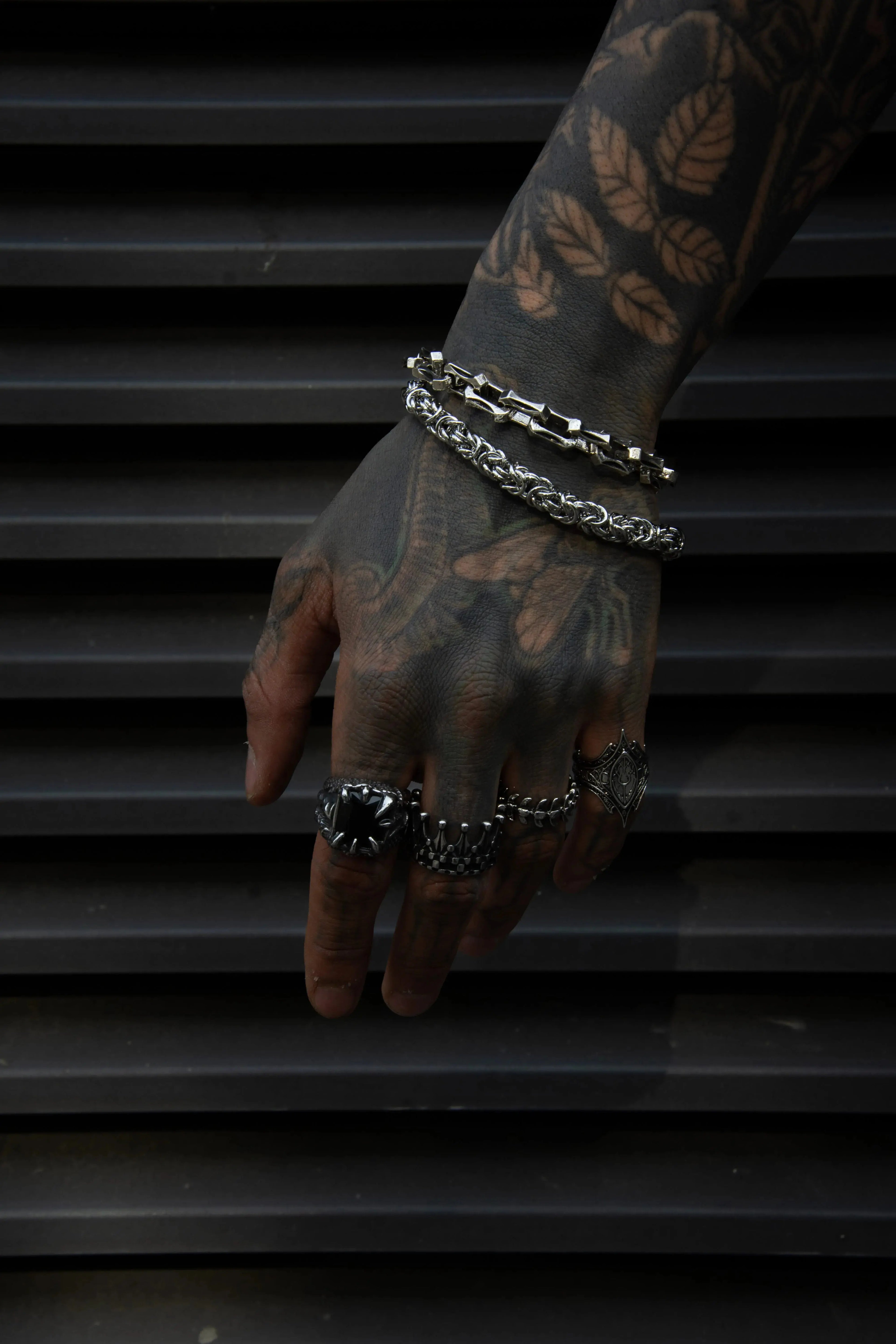 Bracelet chaîne en acier inoxydable argenté style bijou rock et biker porté par un homme tatoué et avec des belles bagues 