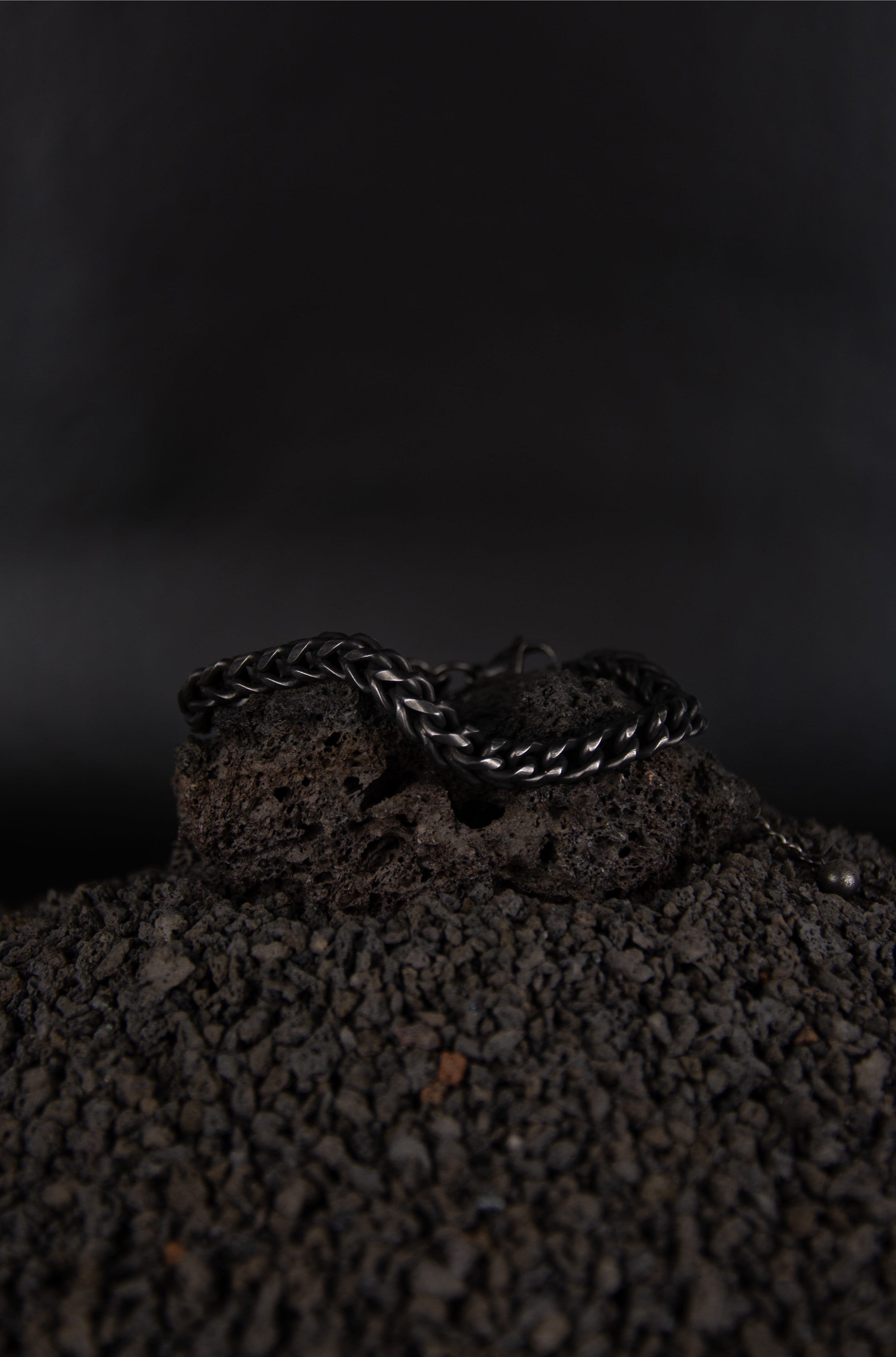 Un bracelet chaine noir en acier inoxydable posé sur de la roche volcanique noir.