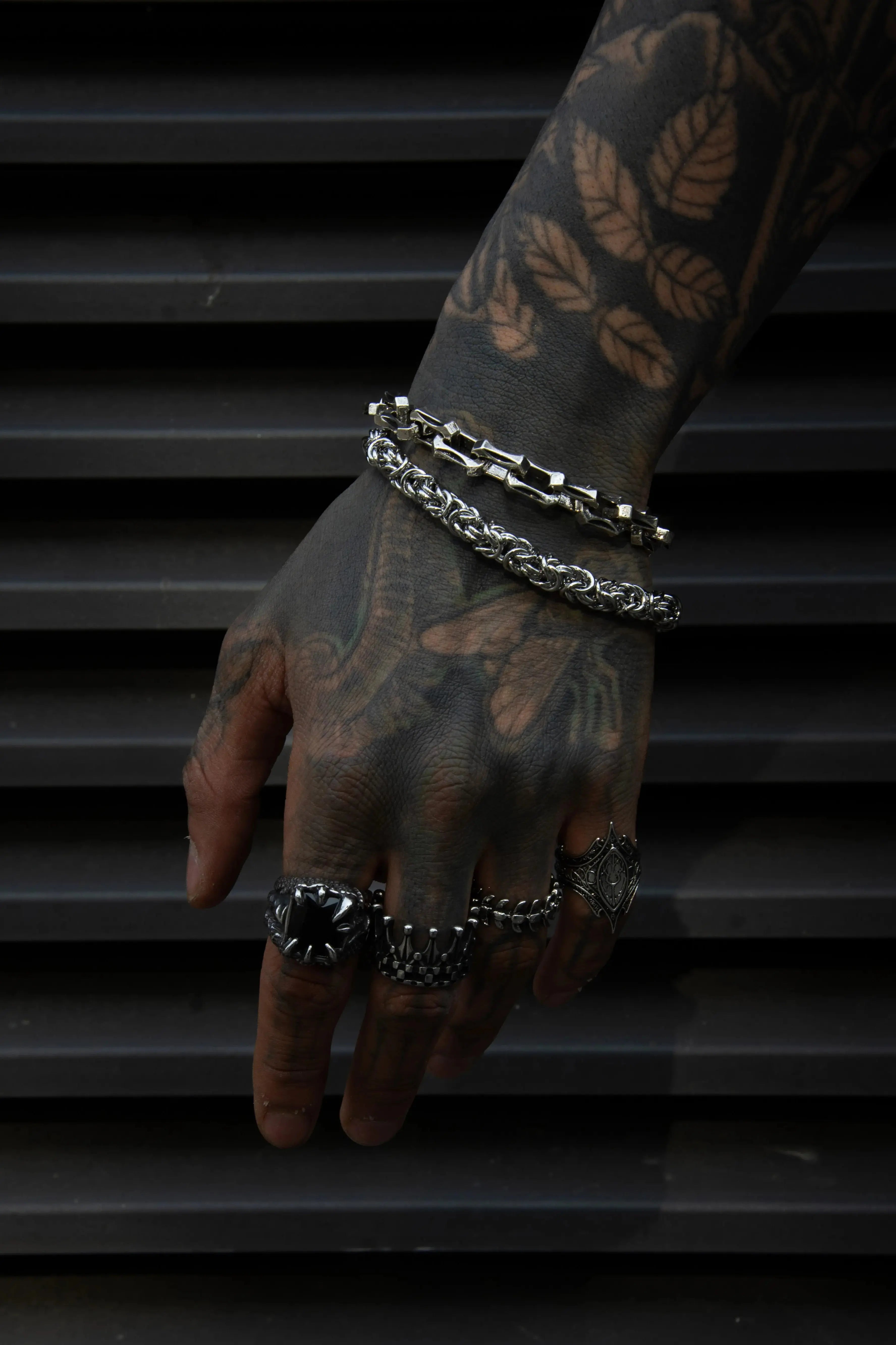 Une main complètement tatoué qui porte des bracelet en acier inoxydable tendance et des bagues et chevalière rock