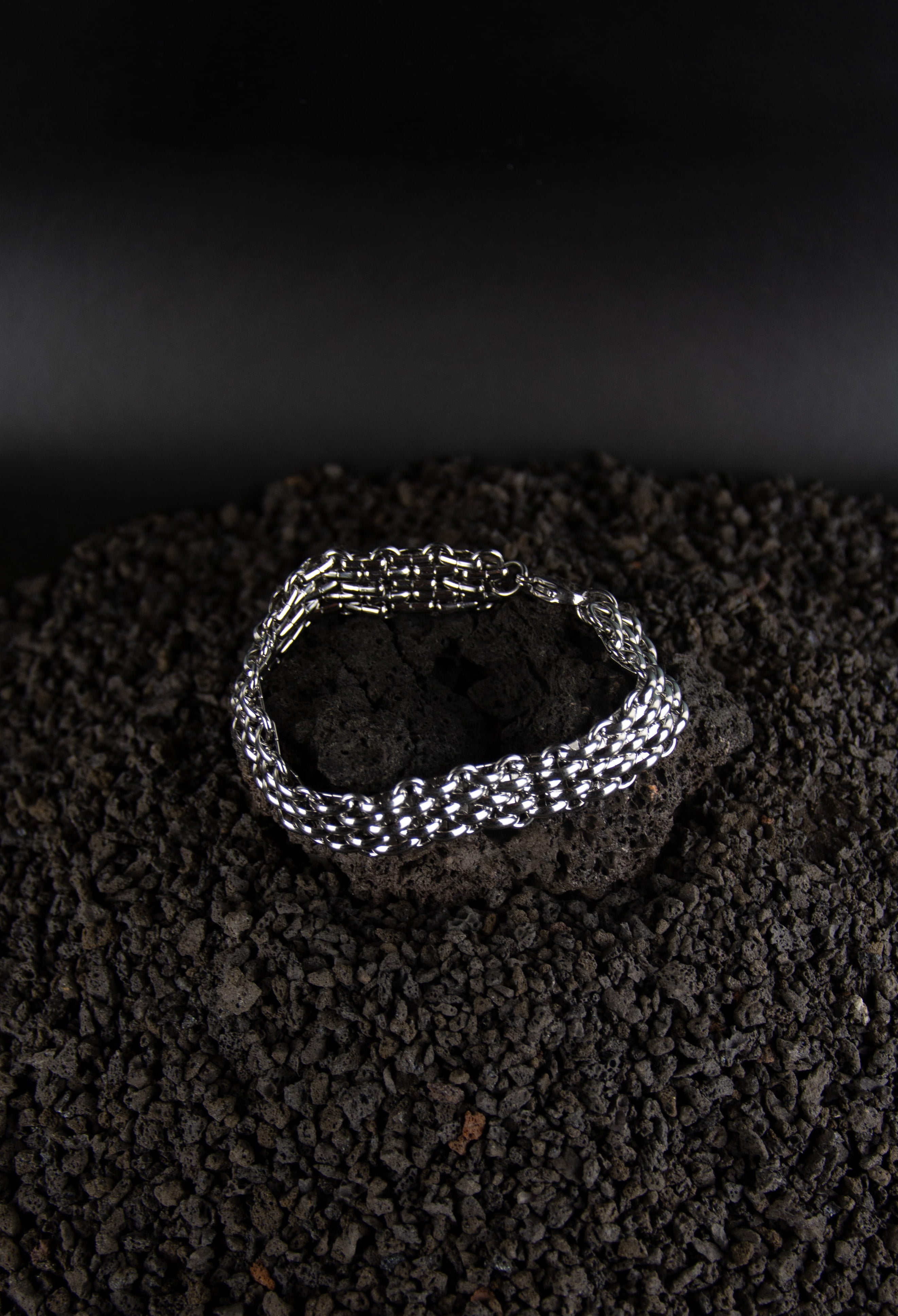 Chaîne bracelet plate en acier inoxydable posé sur roche volcanique noir