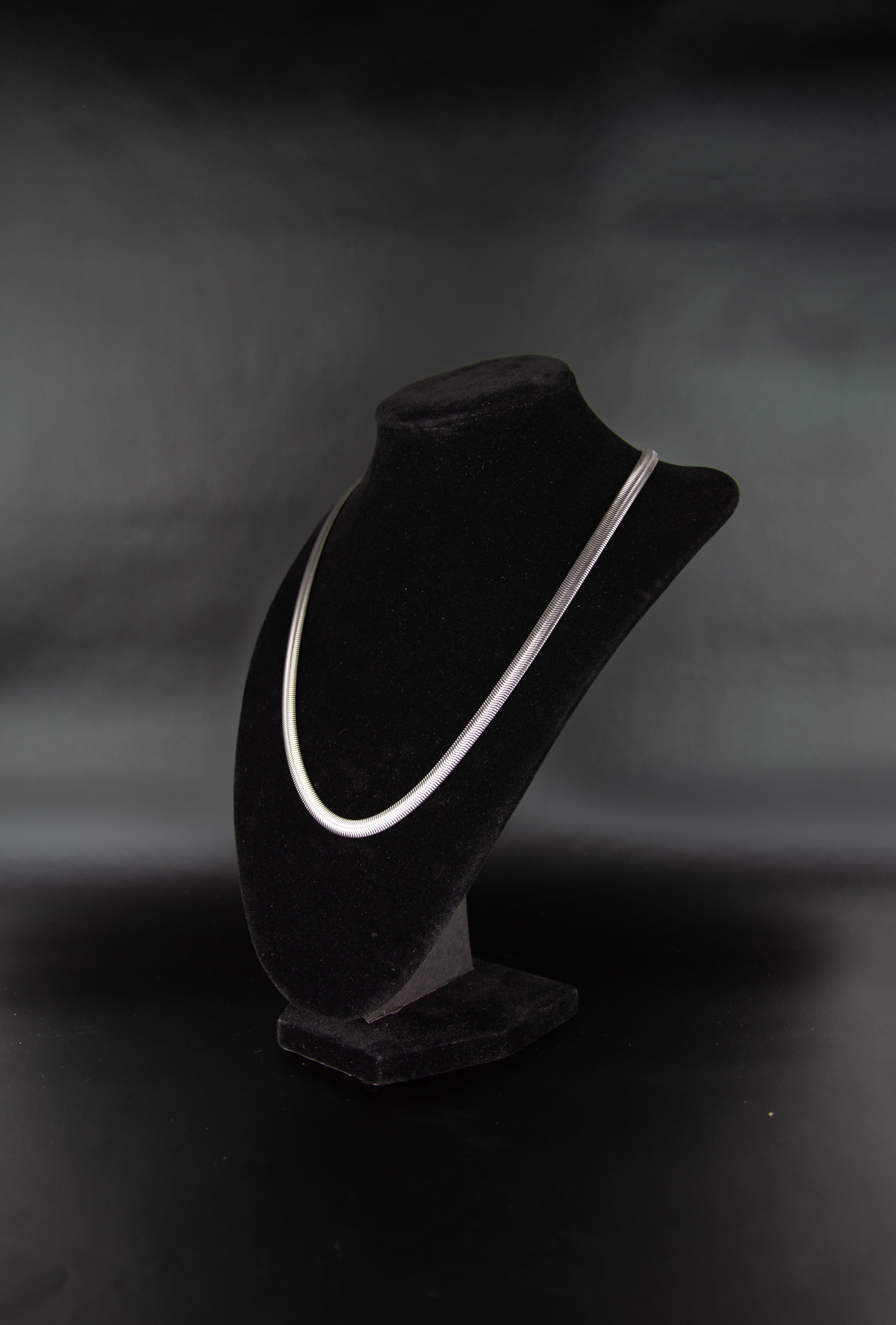 Collier chaîne serpent en acier inoxydable posé sur un présentoir à bijoux en velour noir. 