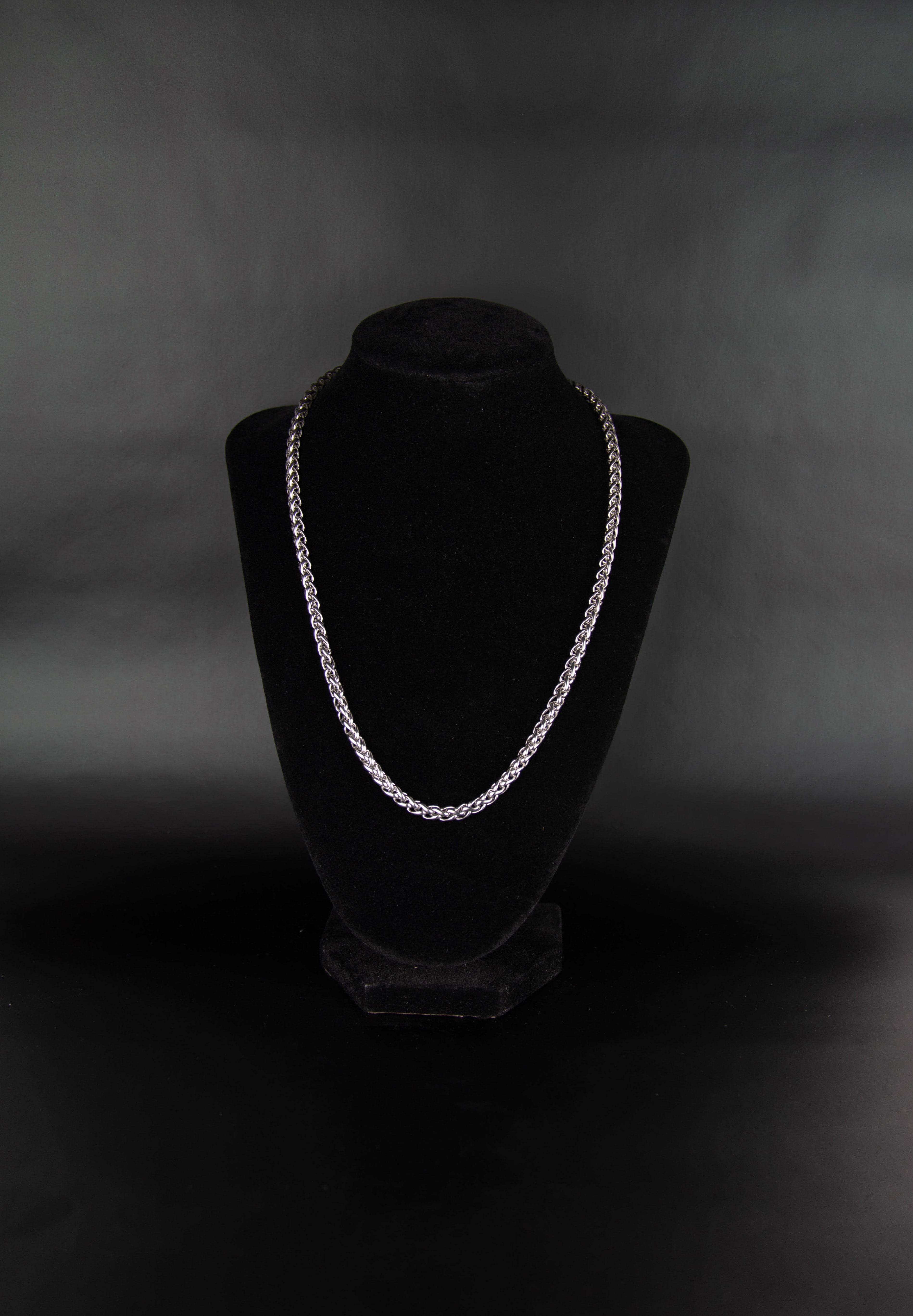 Collier chaîne torsadée en acier inoxydable posé sur un présentoir à bijoux en velour noir sur fond noir.