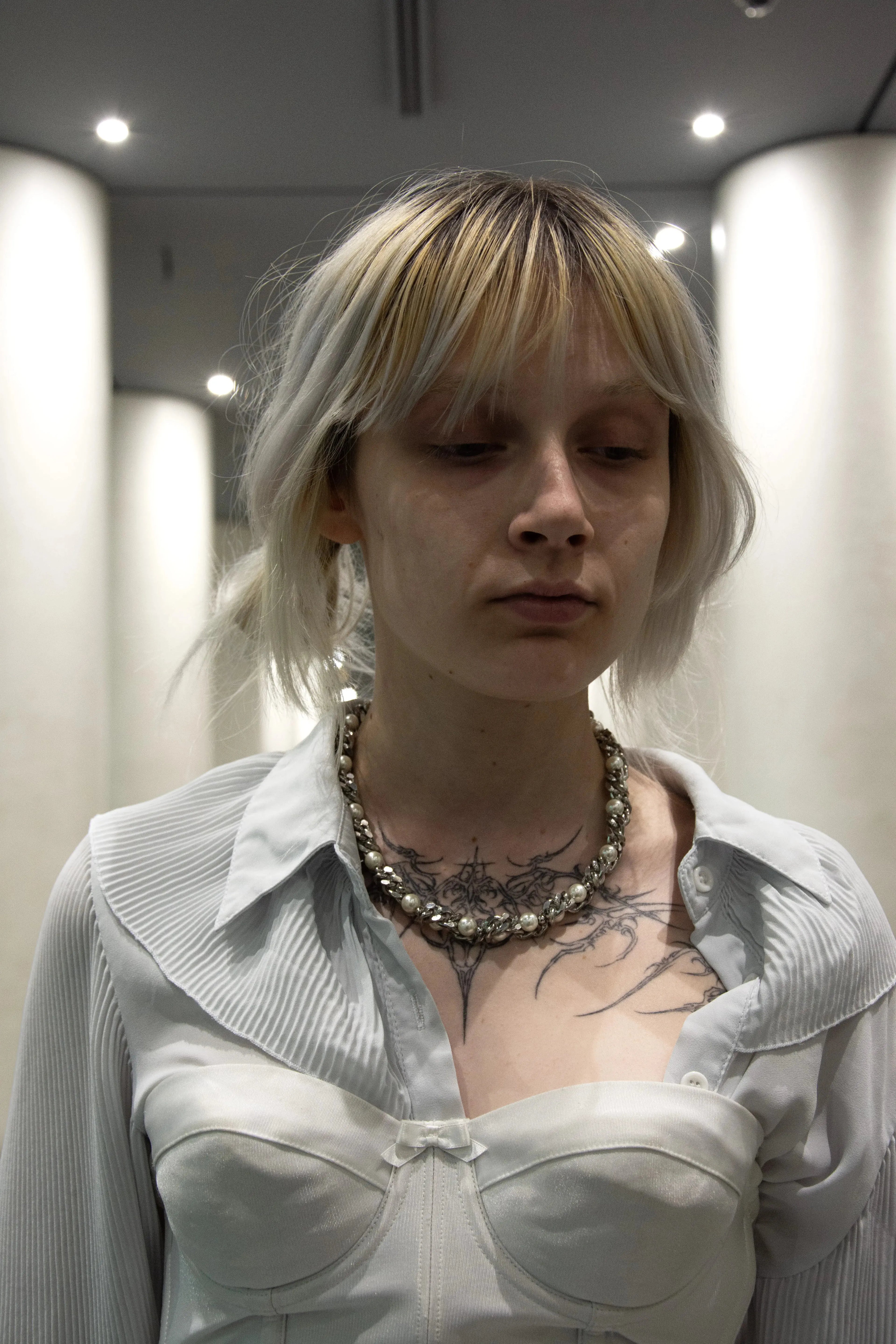 Collier de perle et chaine acier inoxydable mixte porté par une femme au teint pale et au décolleté tatoué 