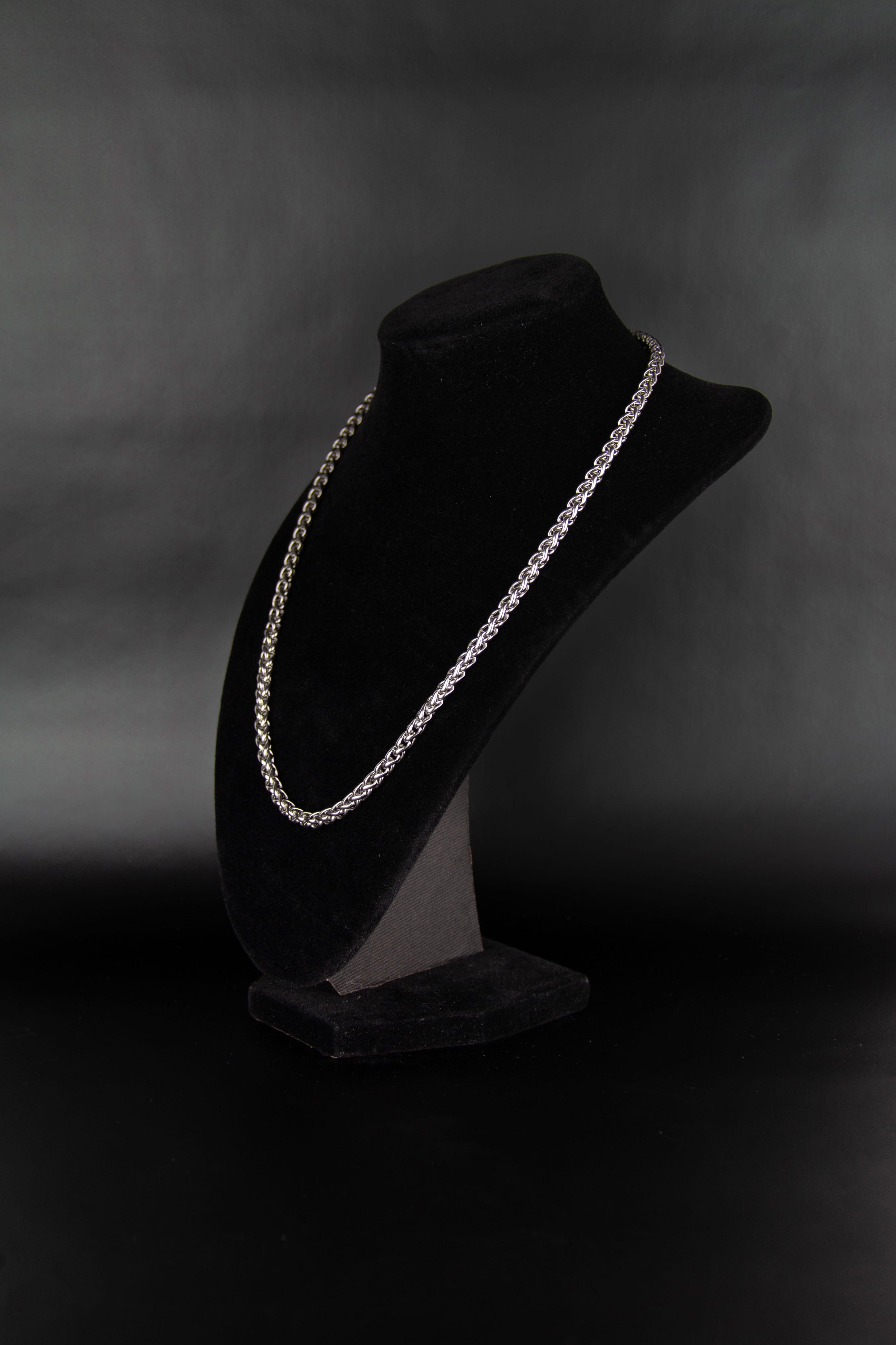 Collier chaîne torsadée en acier inoxydable posé sur un présentoir à bijoux en velour noir de trois quarts sur fond noir.