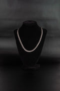 Collier chaine maillons cubain en acier inoxydable posé sur un présentoir à bijoux en velours noir et fond noir. 
