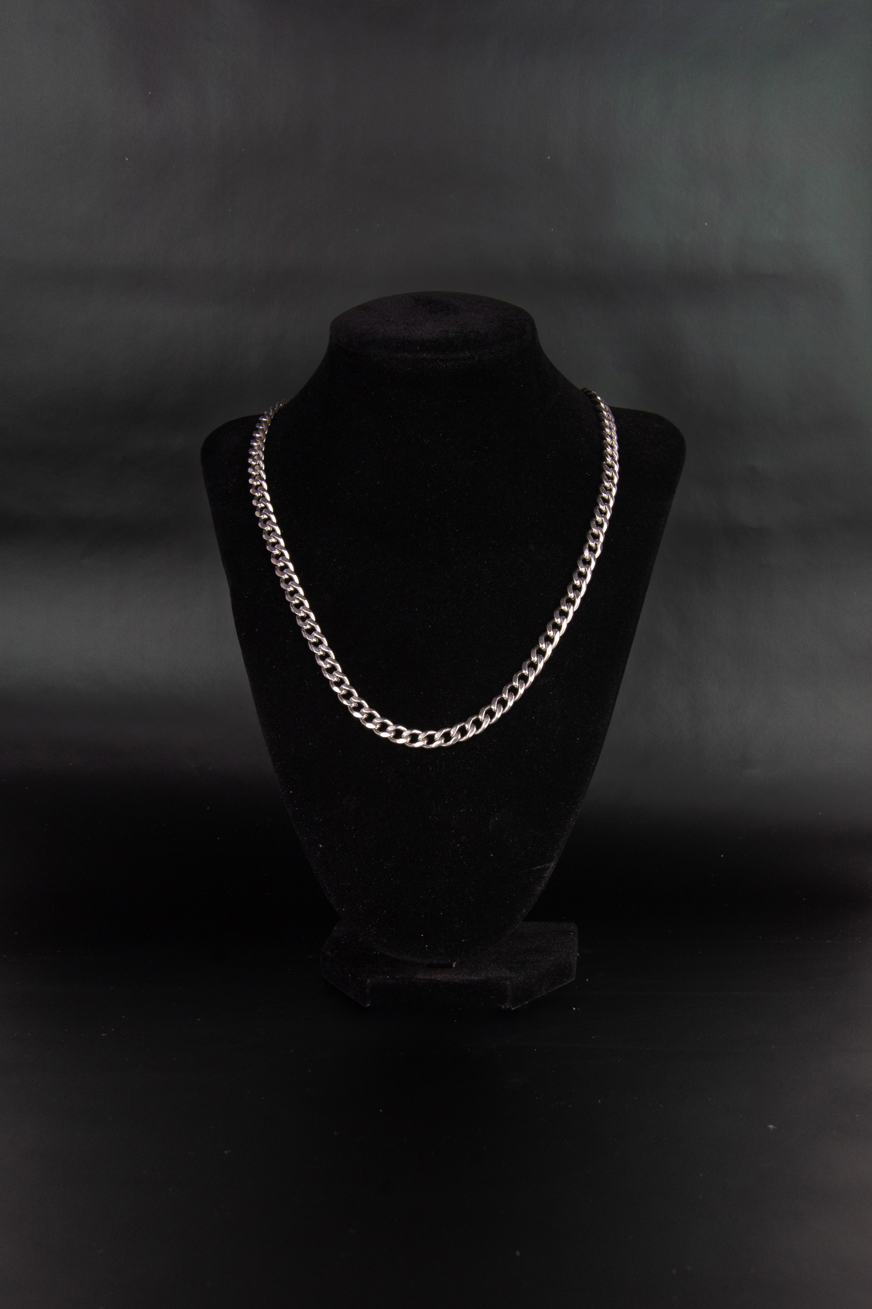 Collier chaine maillons cubain en acier inoxydable posé sur un présentoir à bijoux en velours noir et fond noir. 