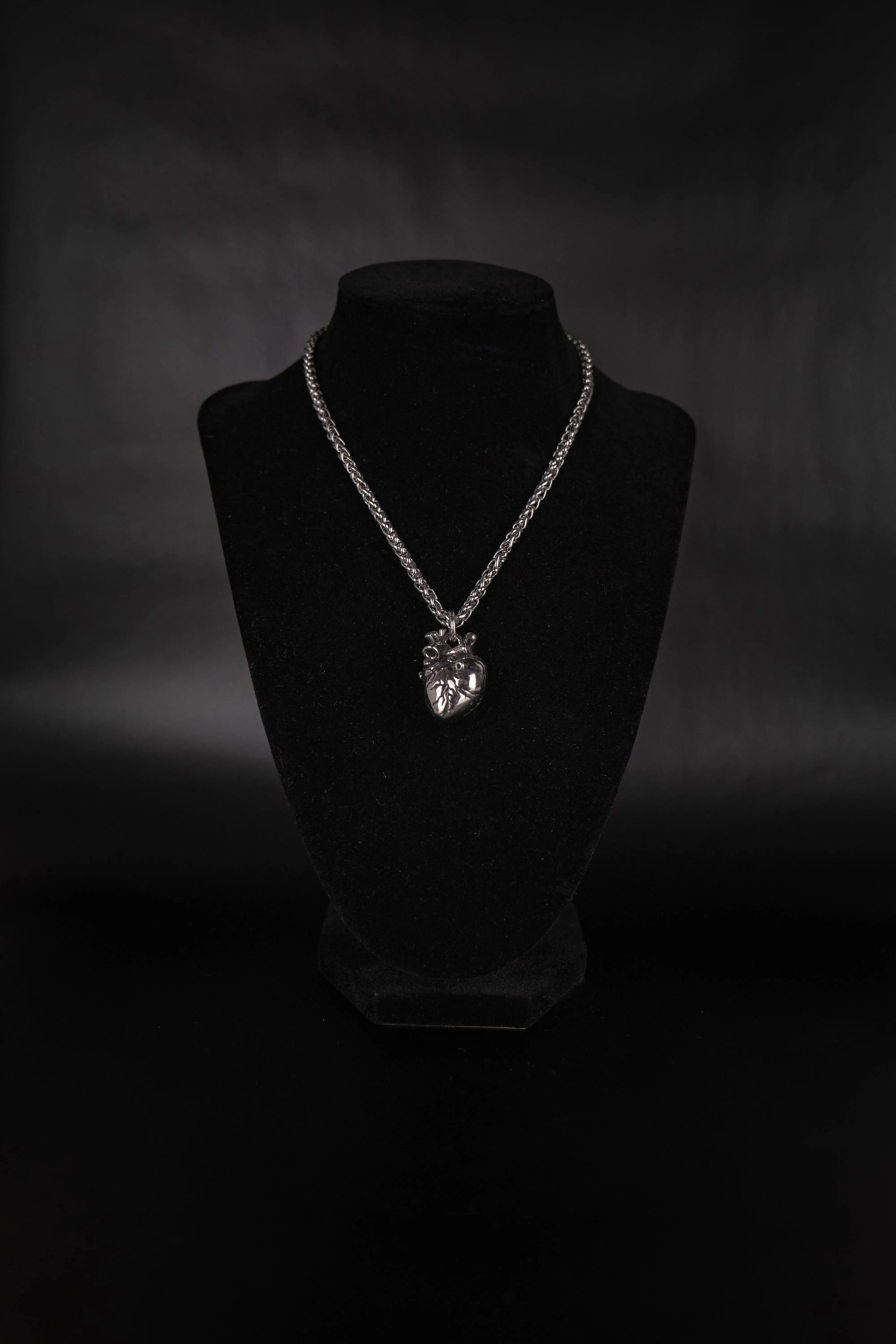 
un collier avec pendentif coeur en acier inoxydable pour homme et femme posé sur un présentoir en velours noir