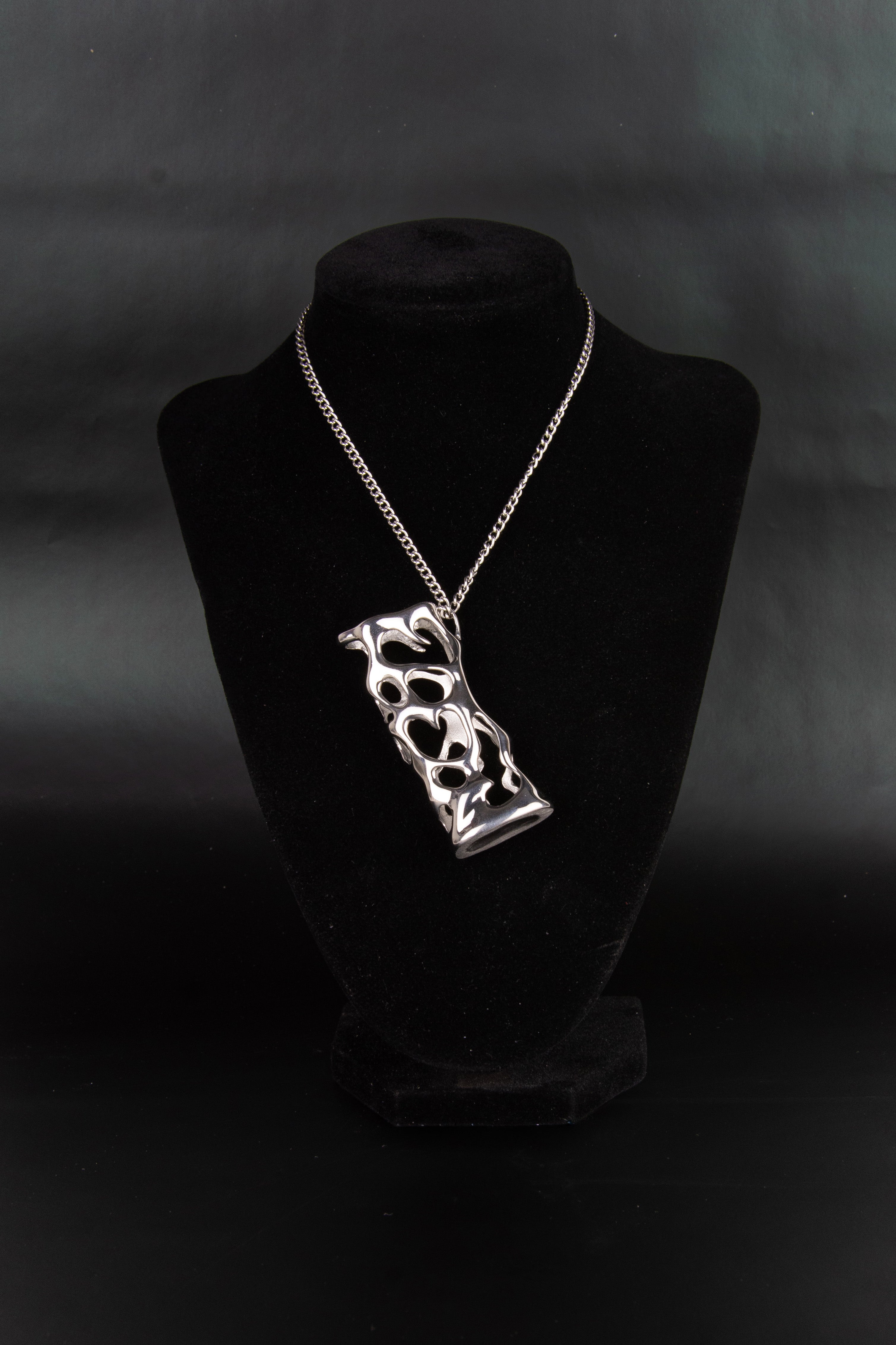 Collier étui à briquet en acier inoxydable posé sur un présentoir en velours noir.
