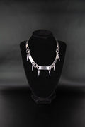 Collier ras de cou avec piques et métallique tab pour lacet de chaussure posé sur un présentoir à bijoux en velours noir et fond noir. 