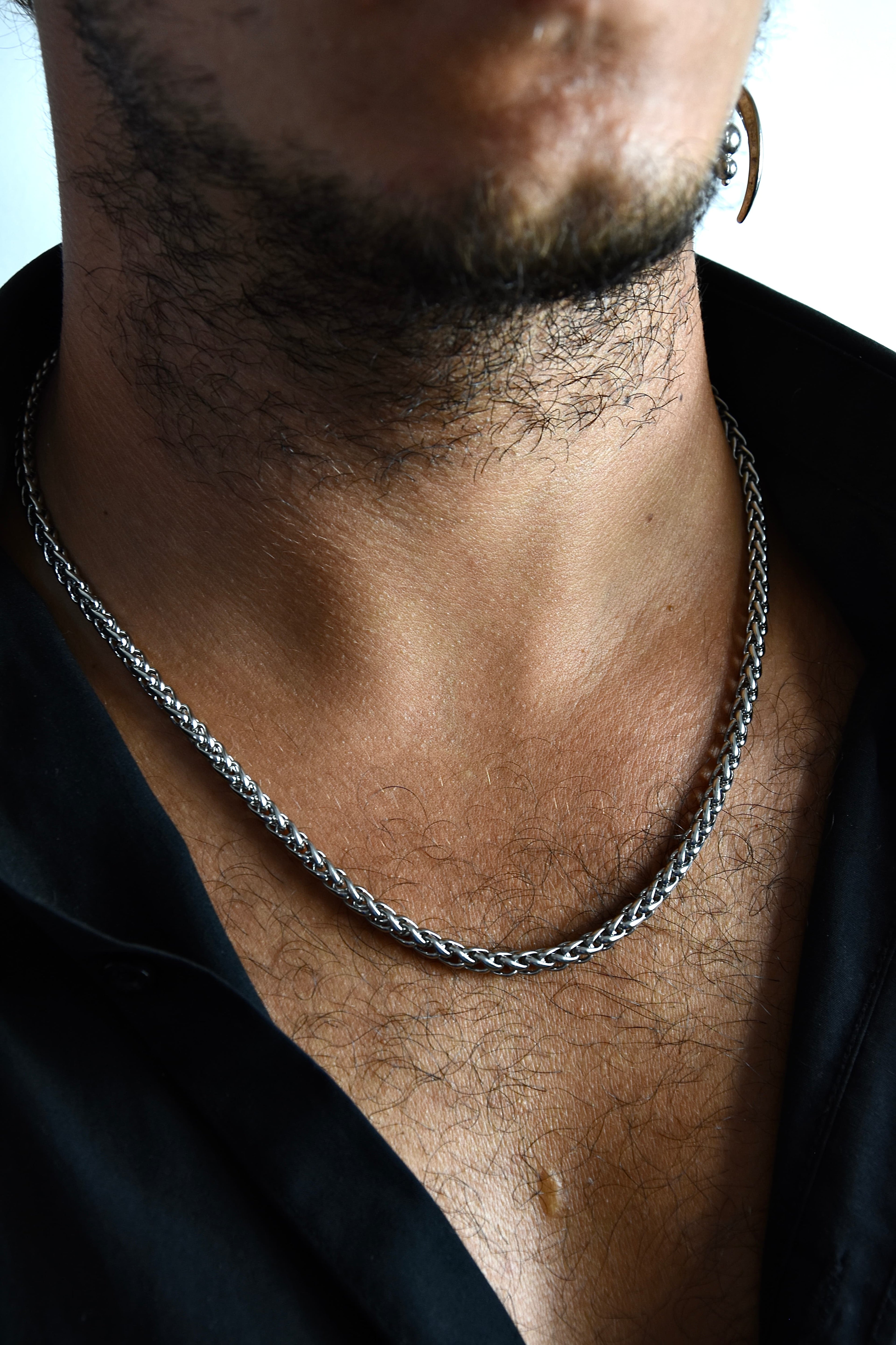 Collier chaîne torsadée en acier inoxydable porté pas un homme avec le col de chemise noir ouverte.
