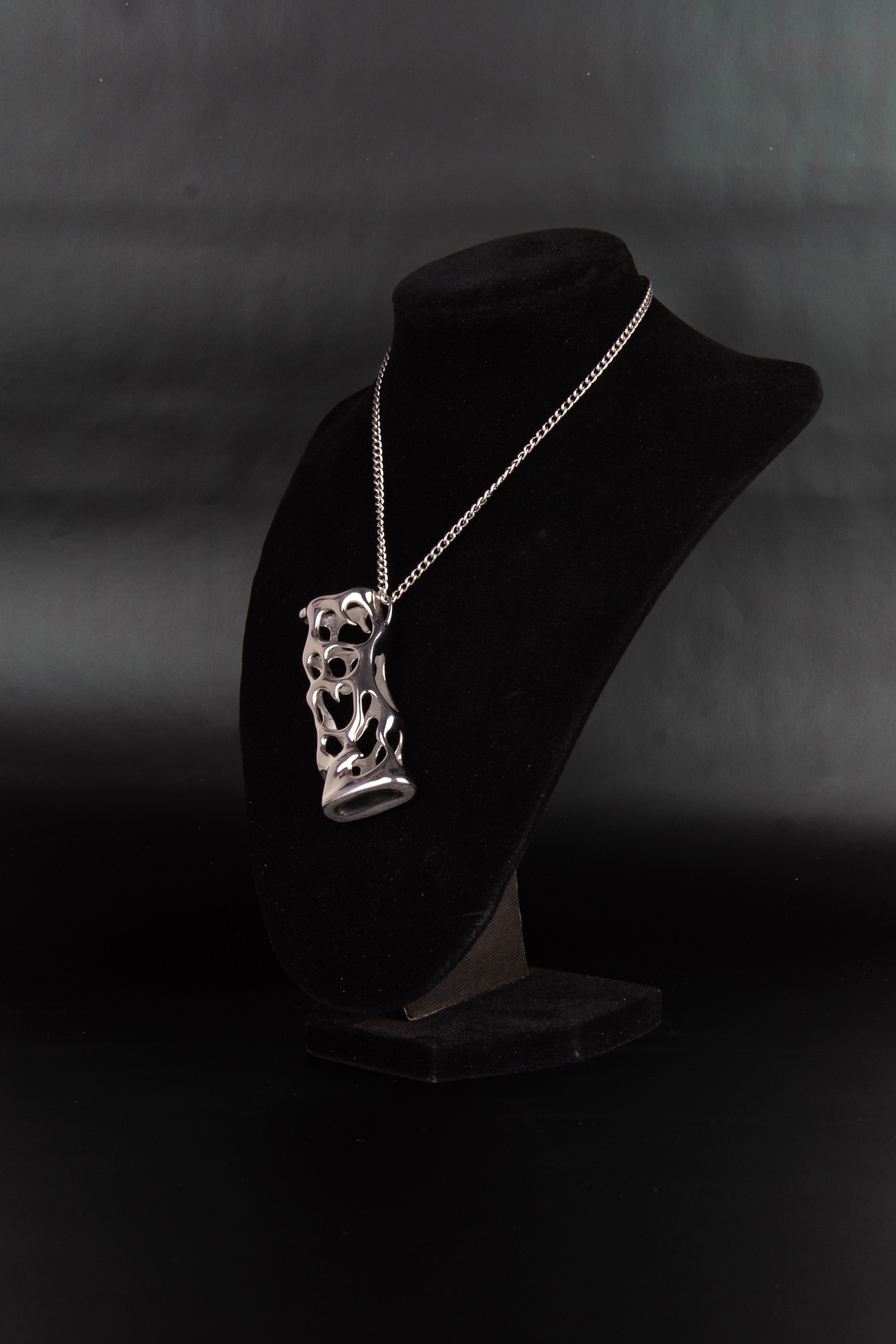 Collier étui à briquet en acier inoxydable posé sur un présentoir en velours noir de trois quarts.