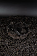 Un bracelet noir avec chaîne torsadée vu du dessus posé sur une roche volcanique noir
