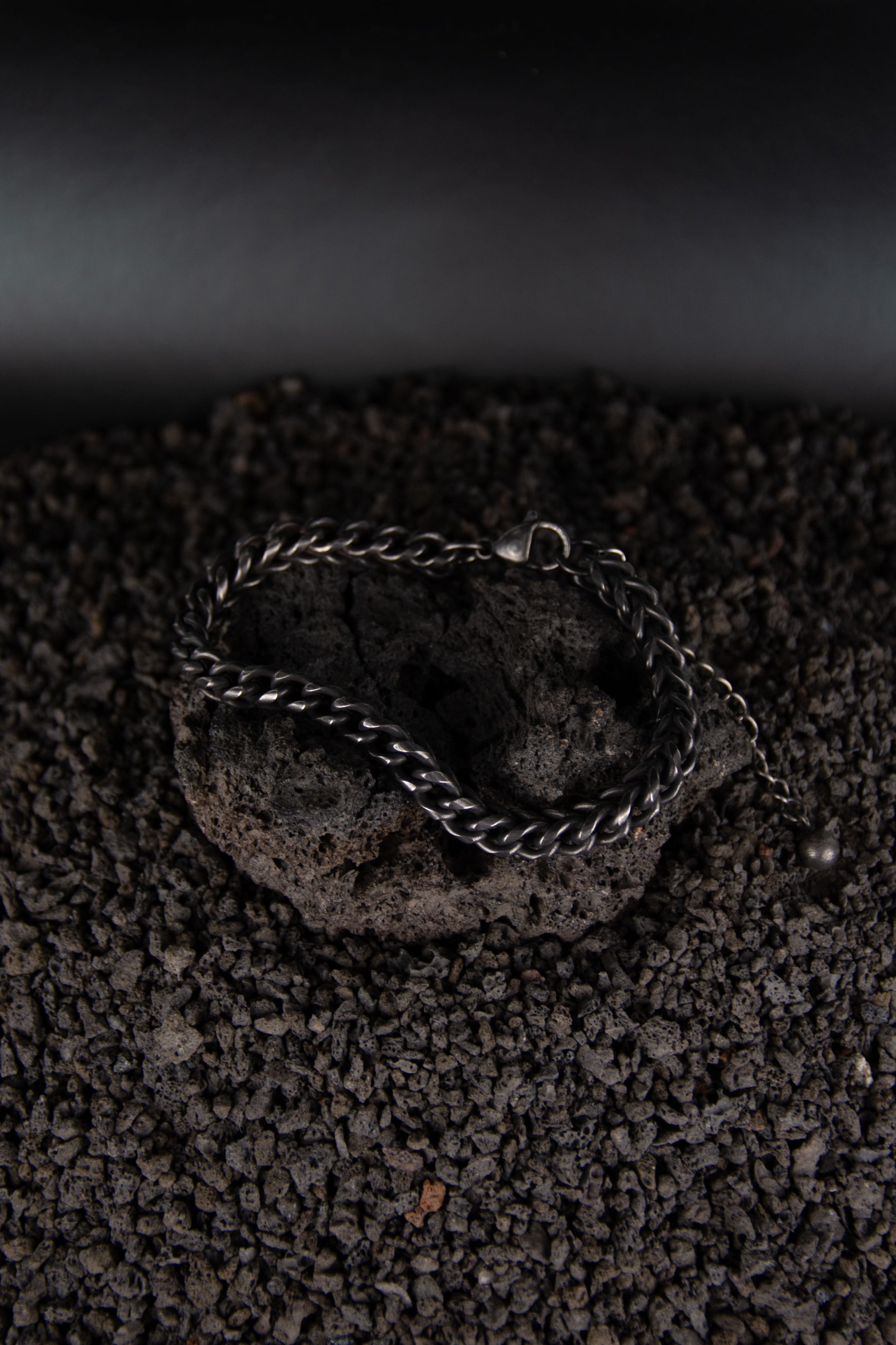Un bracelet noir avec chaîne torsadée vu du dessus posé sur une roche volcanique noir