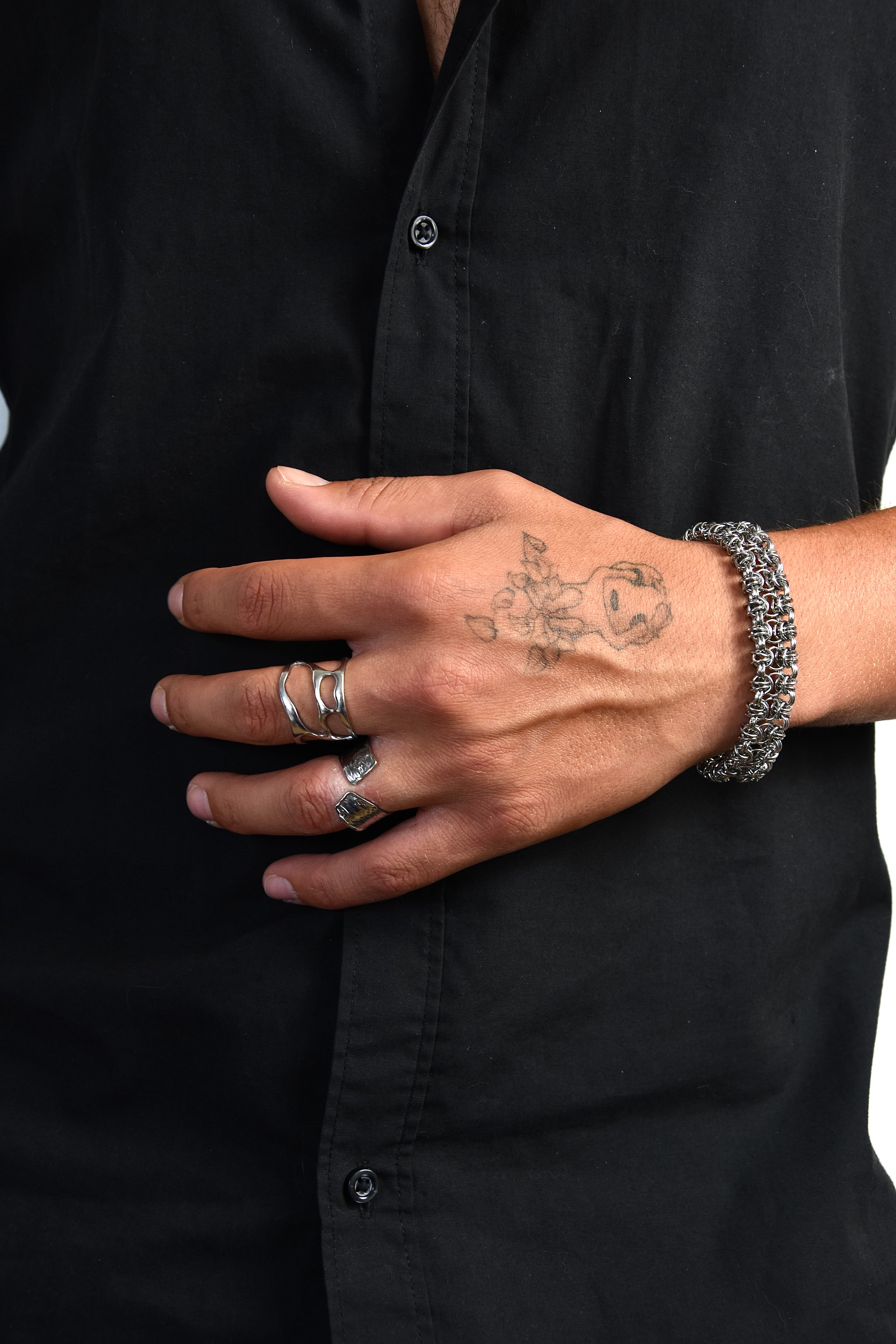 bague style alternatif en acier inoxydable et réglable portée par une main tatouée devant un chemise noir. 