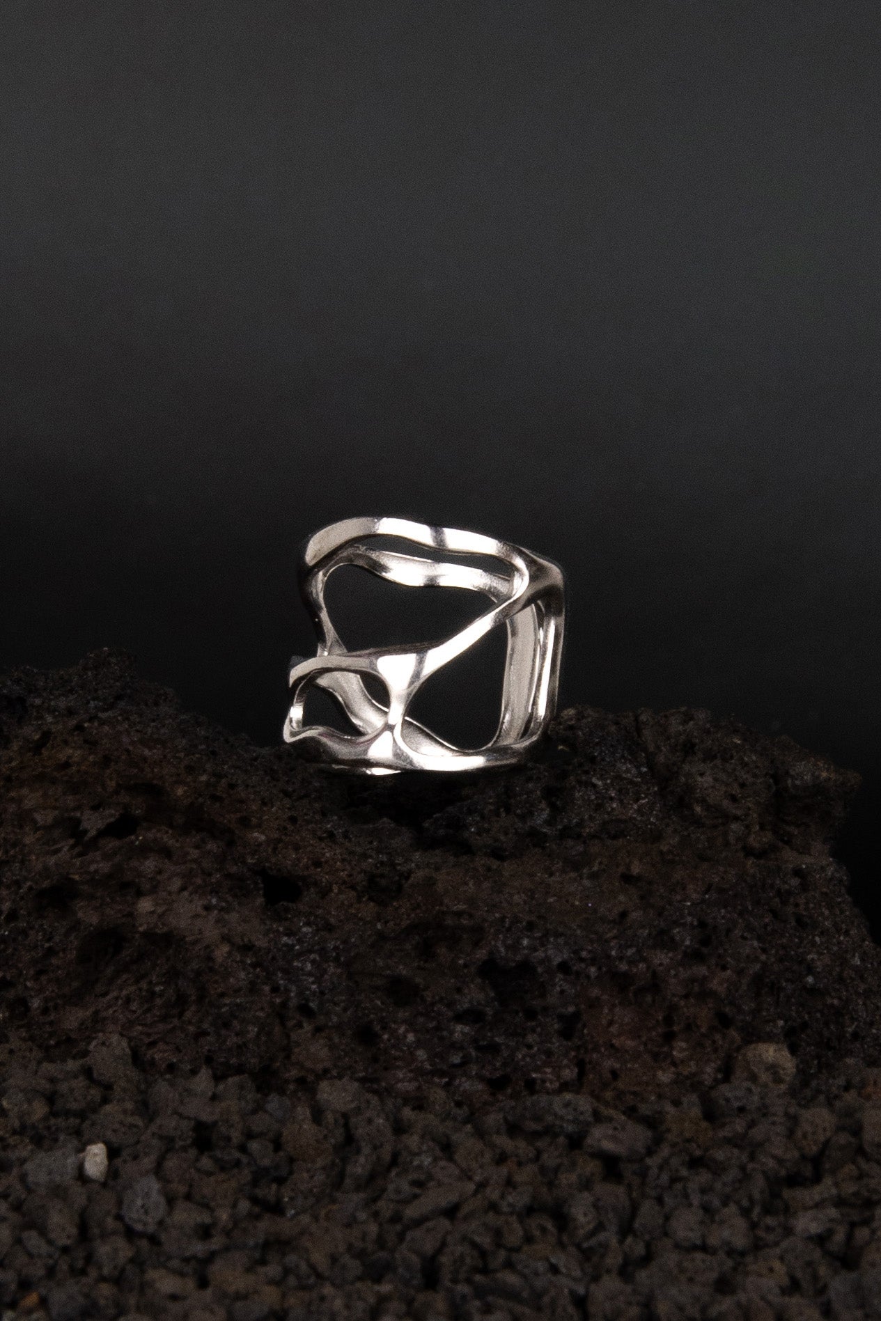 Bague en acier inoxydable posée de trois quarts sur une roche volcanique noir.