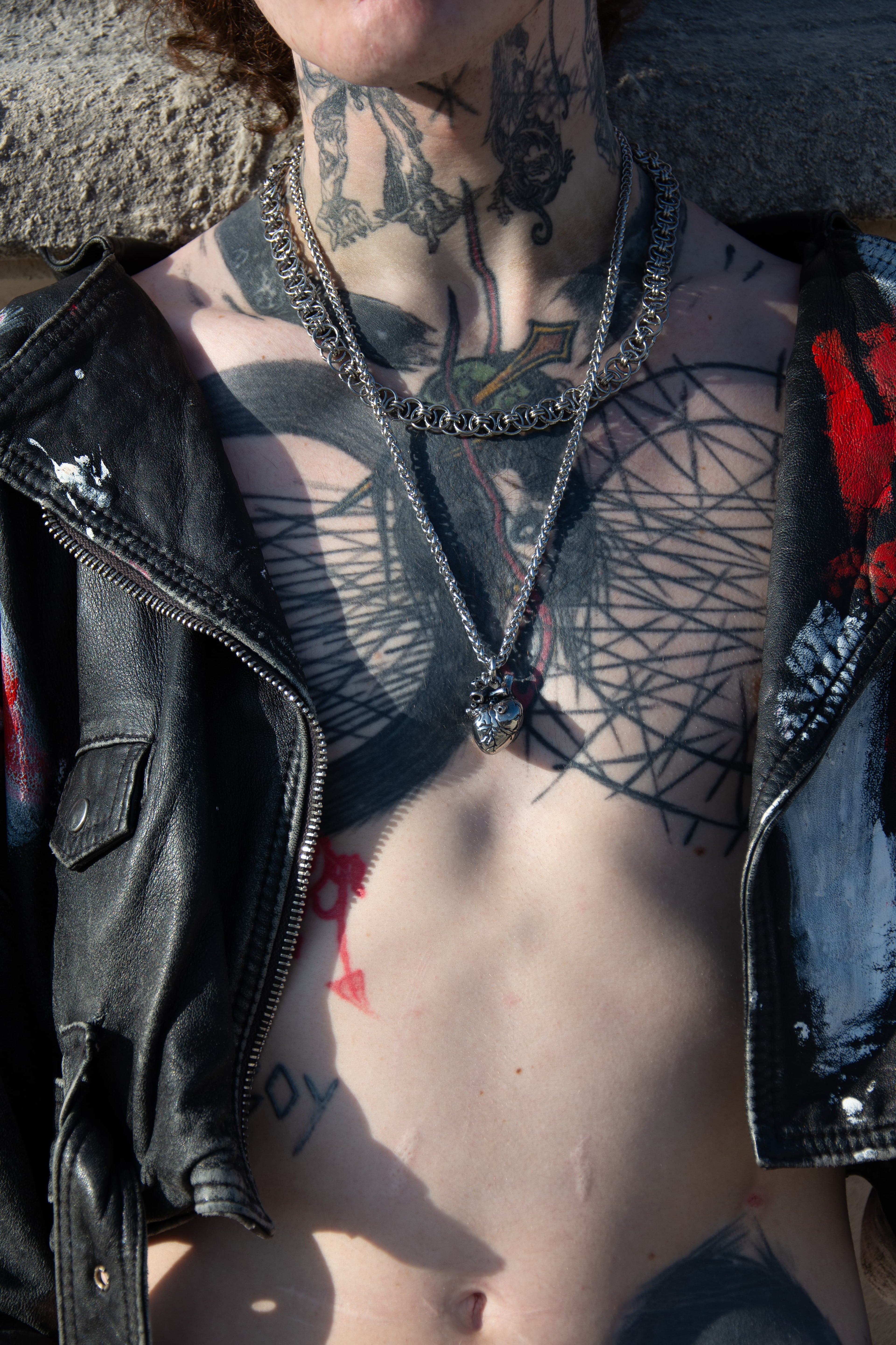 mannequin tatoué et torse nu portant un veste ouverte et des collier en acier inoxydable.