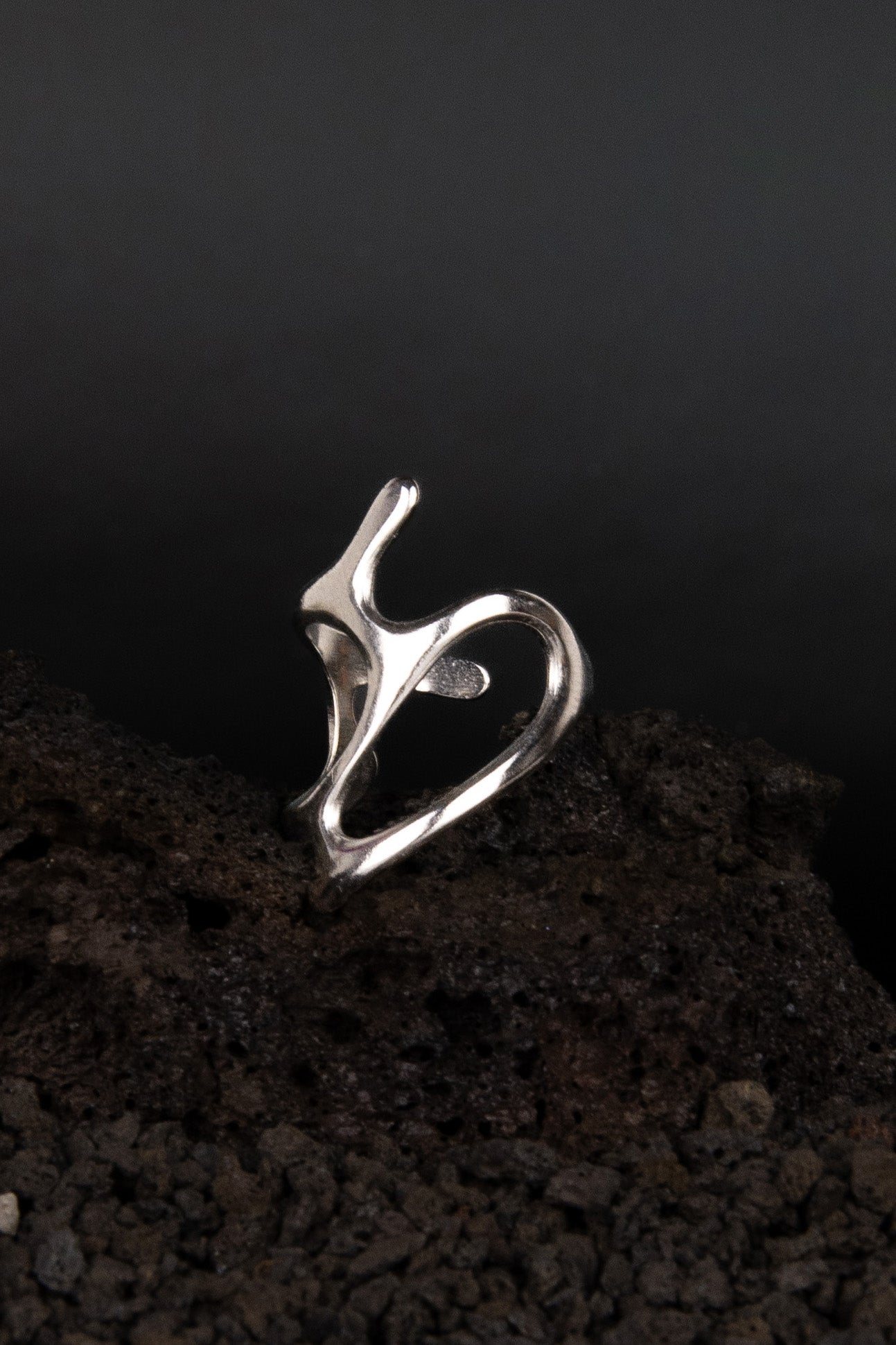 Bague en acier inoxydable en forme de vague métallique posée de trois quarts sur une roche volcanique noir.