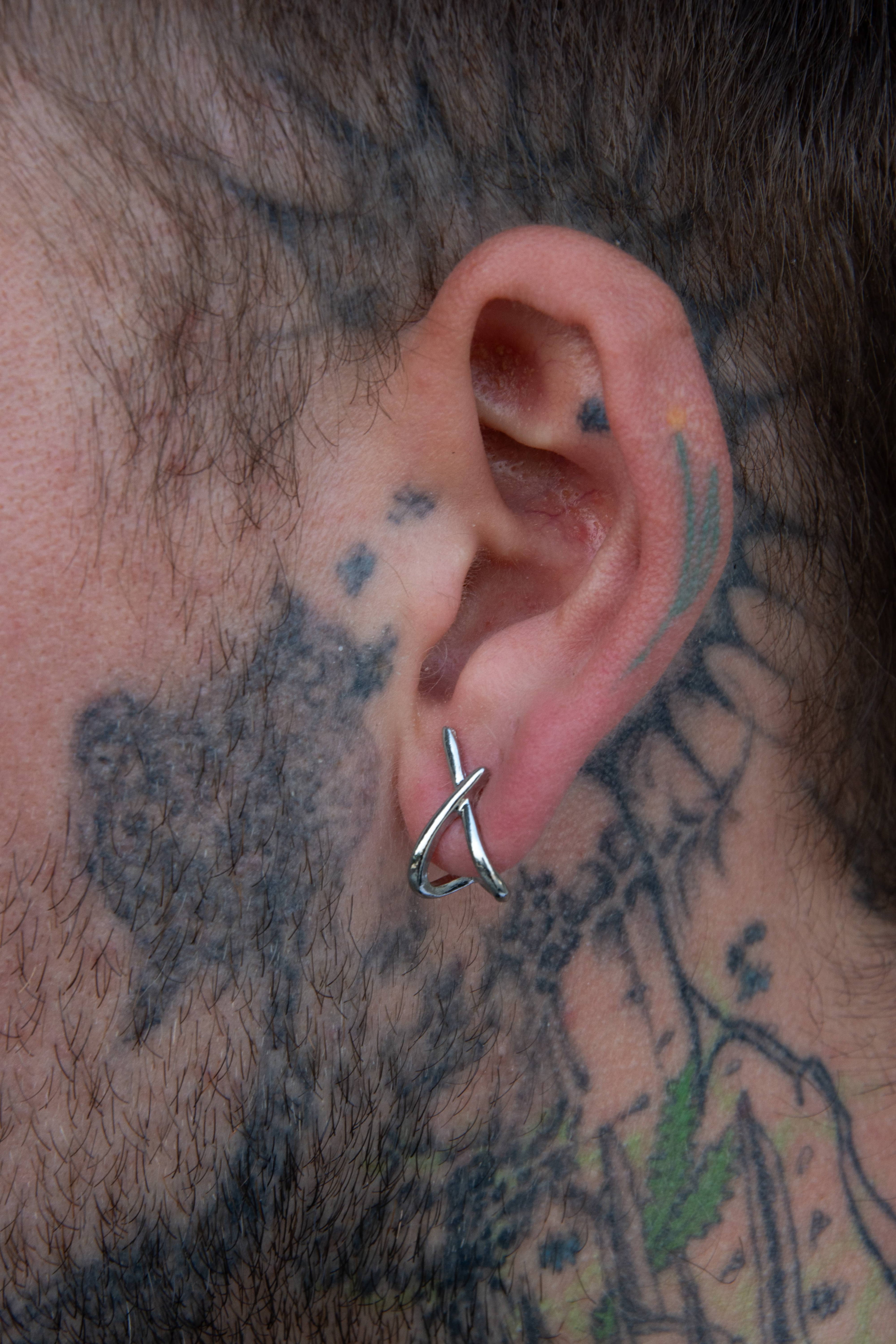 Paire de boucle d’oreille en forme de X symétrique portée par un mannequin tatoué