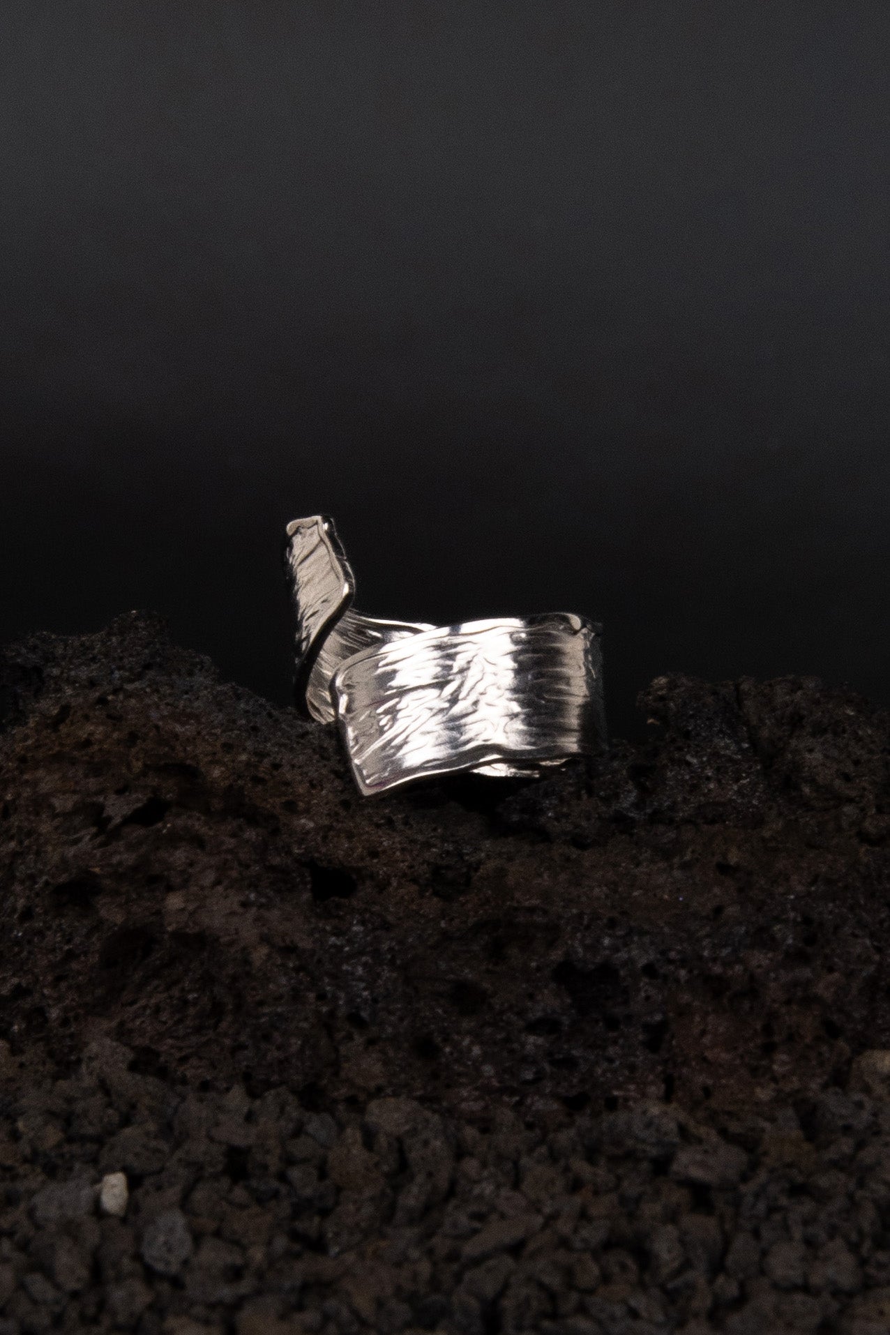 Bague en acier inoxydable avec une texture similaire au bois coupé posée de trois quarts sur de la roche volcanique noir.
