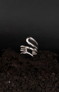 Bague asymétrique ouverte et réglable en acier inoxydable posée sur une roche volcanique noir.