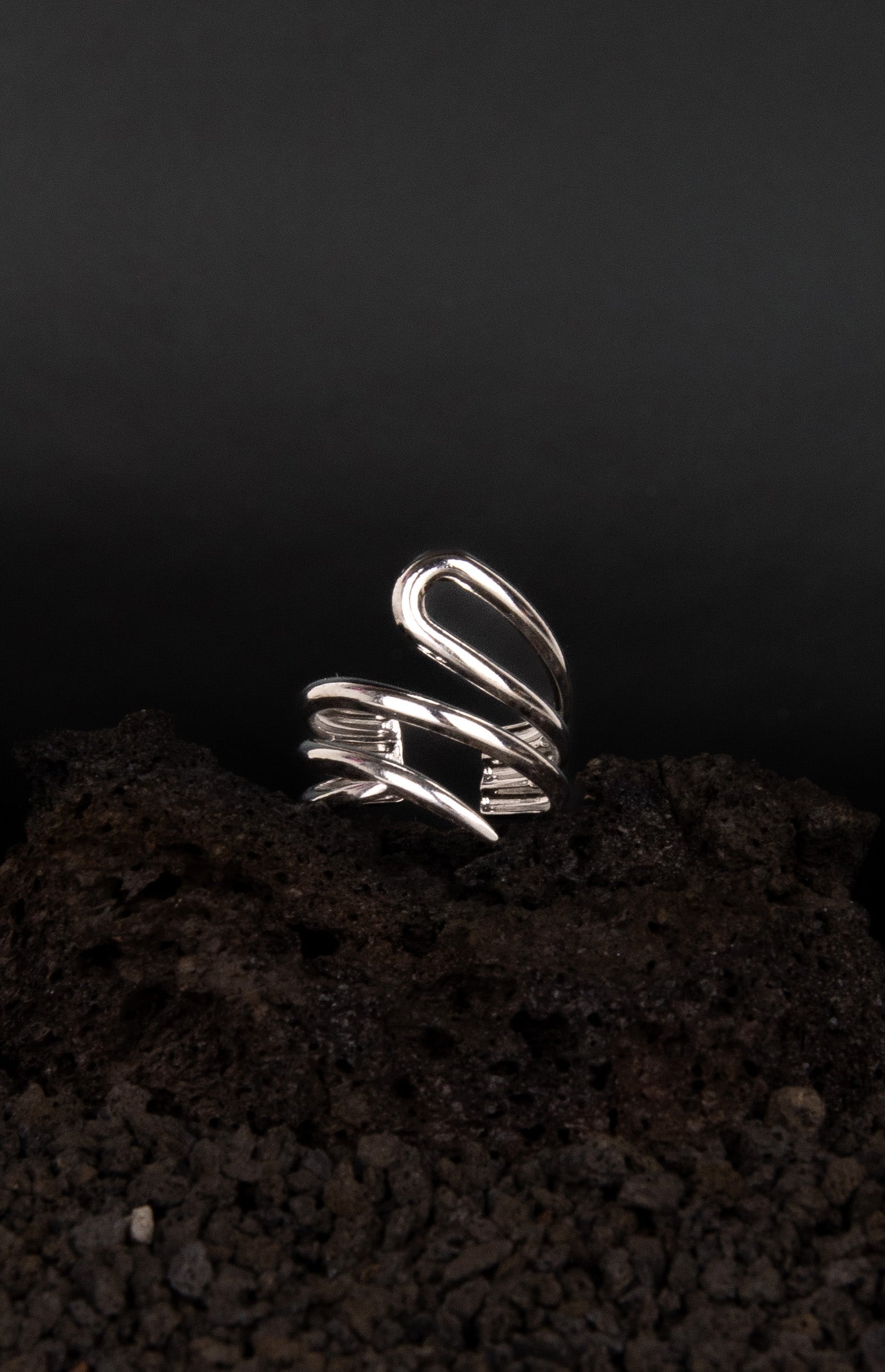 Bague asymétrique ouverte et réglable en acier inoxydable posée sur une roche volcanique noir.