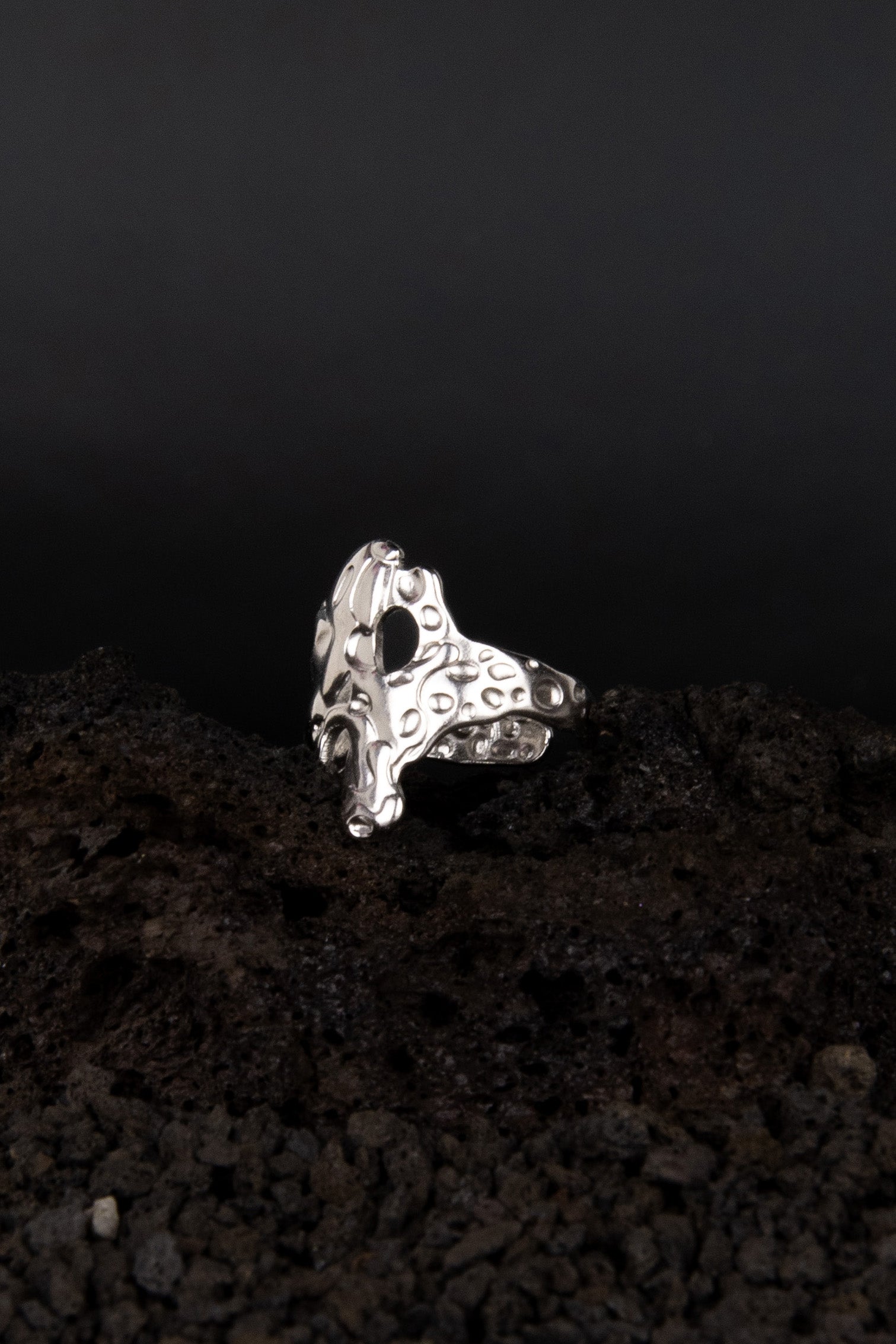 bague réglable en acier inoxydable effet métal fondu posée de trois quarts sur de la roche volcanique noir.