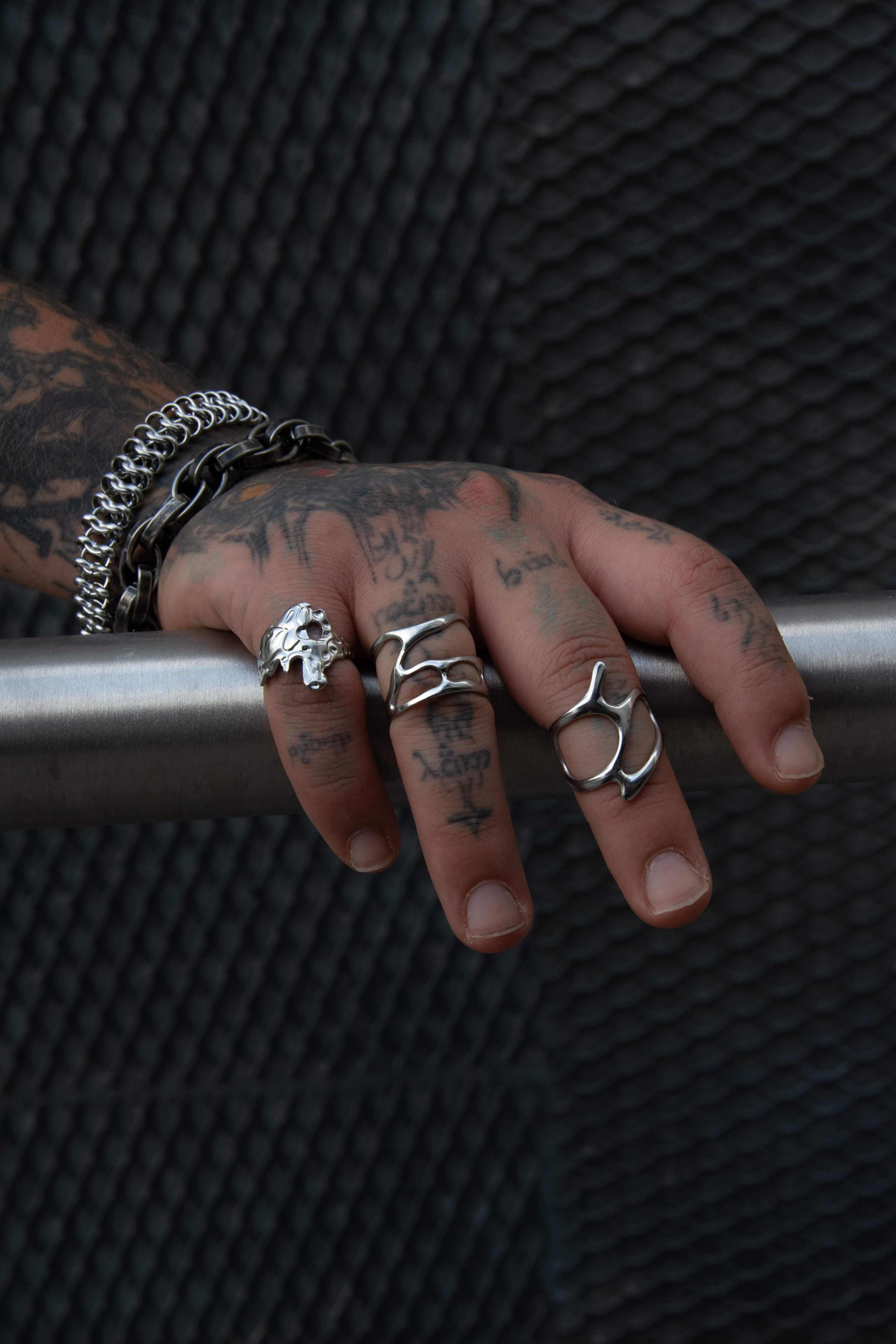Main tatoué portant trois bague assorties en acier inoxydable.